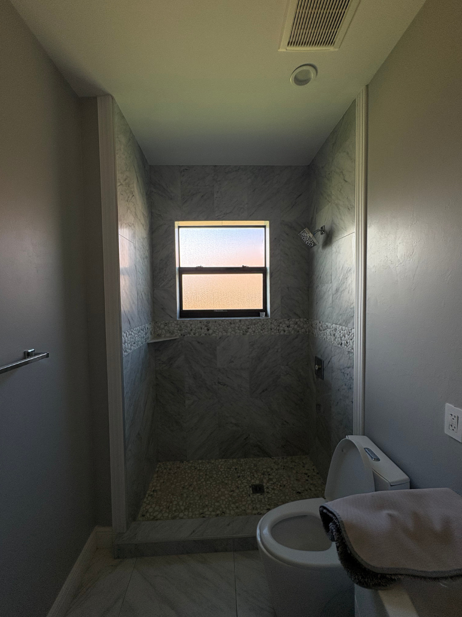 A bathroom with a stone-tiled shower featuring a small rectangular window, next to a white toilet with a gray towel.