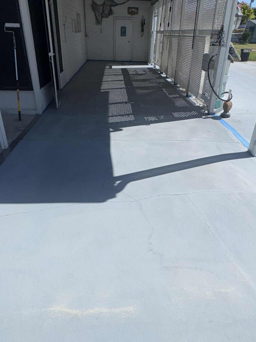 A freshly painted light blue concrete patio under a covered carport with shadows cast by the structure.