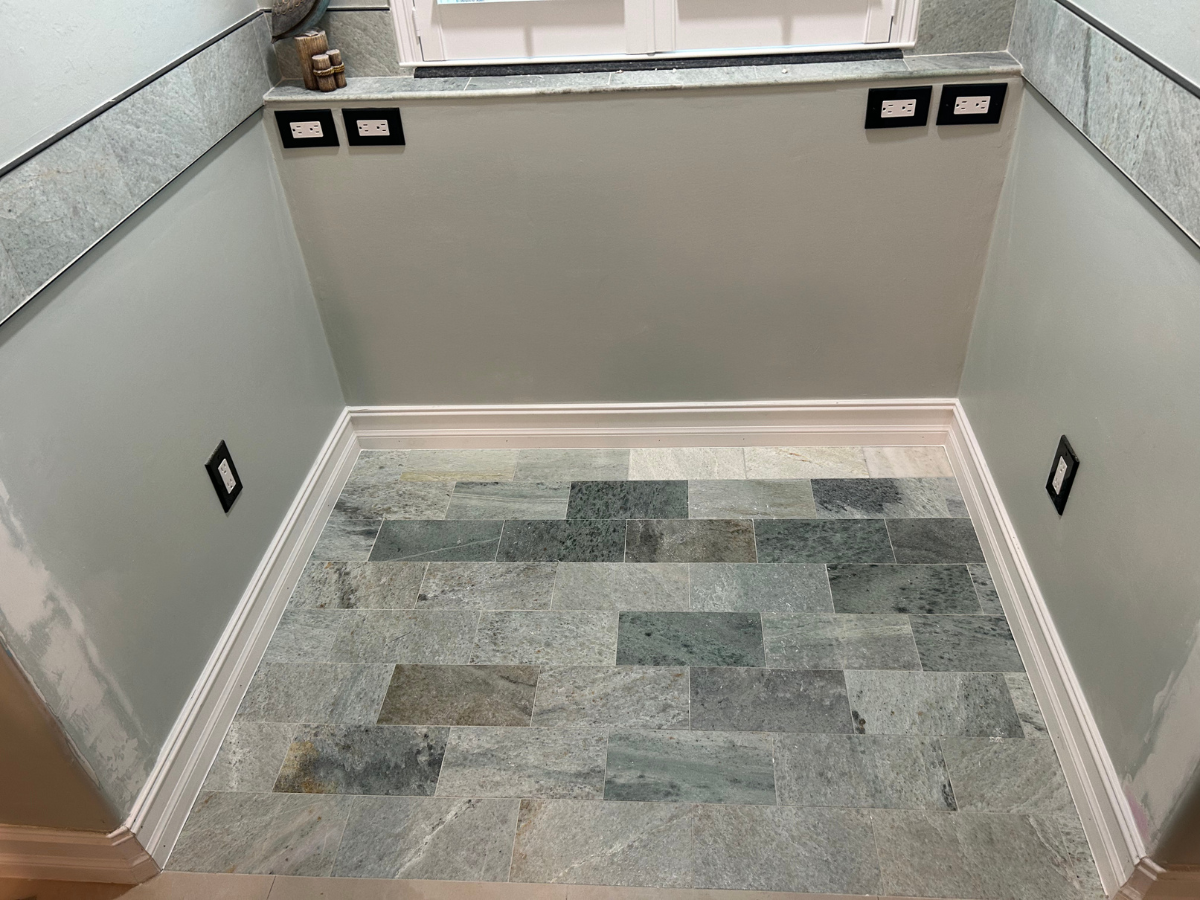 A window nook with grey walls, white trim, and a floor paved with rectangular green and grey stone tiles.
