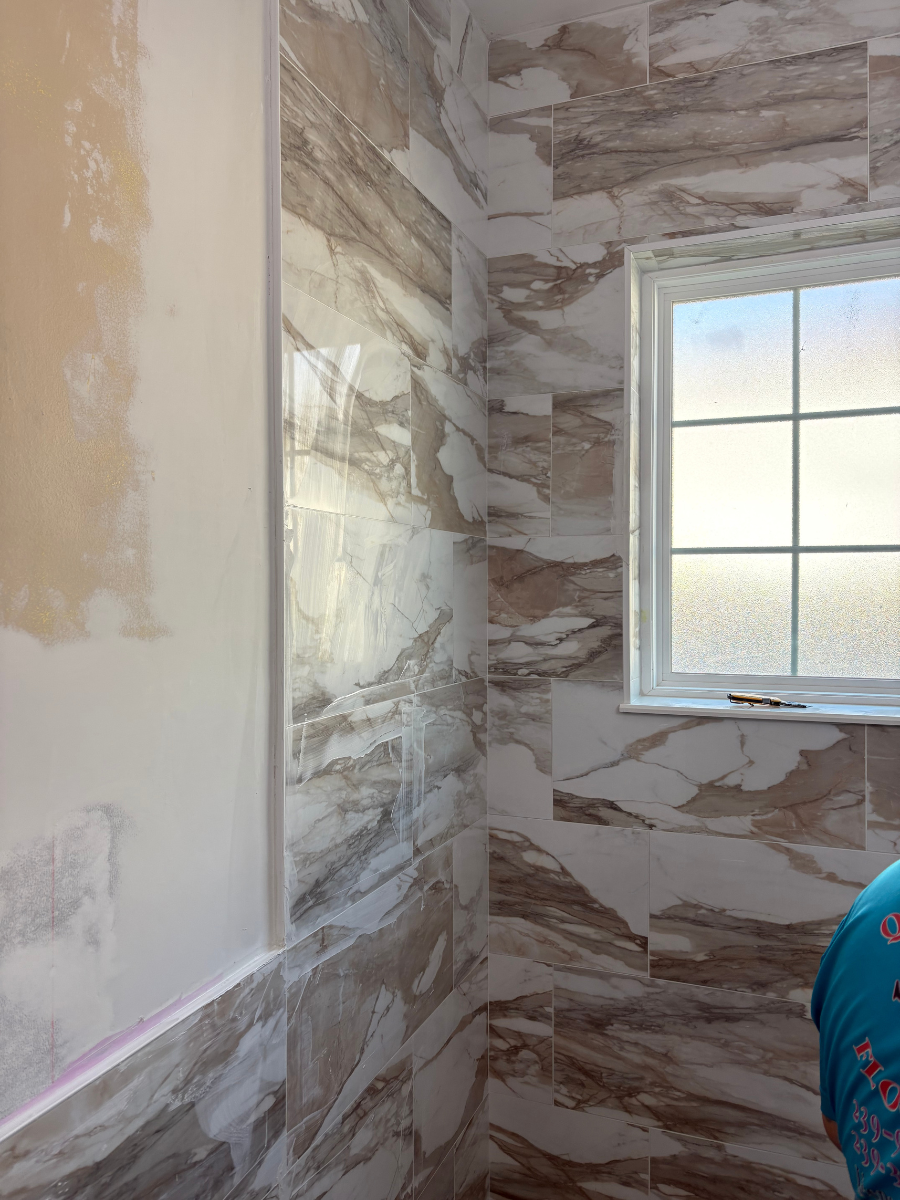 A corner of a room featuring wall tiles with a brown and white marbled pattern and a window with a white grid frame.