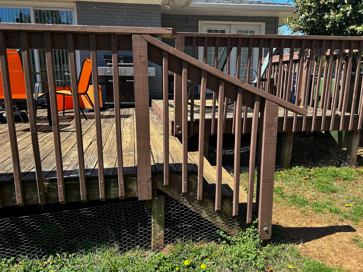 A brown wooden deck with stairs and railings, located outside a house with a grey exterior.