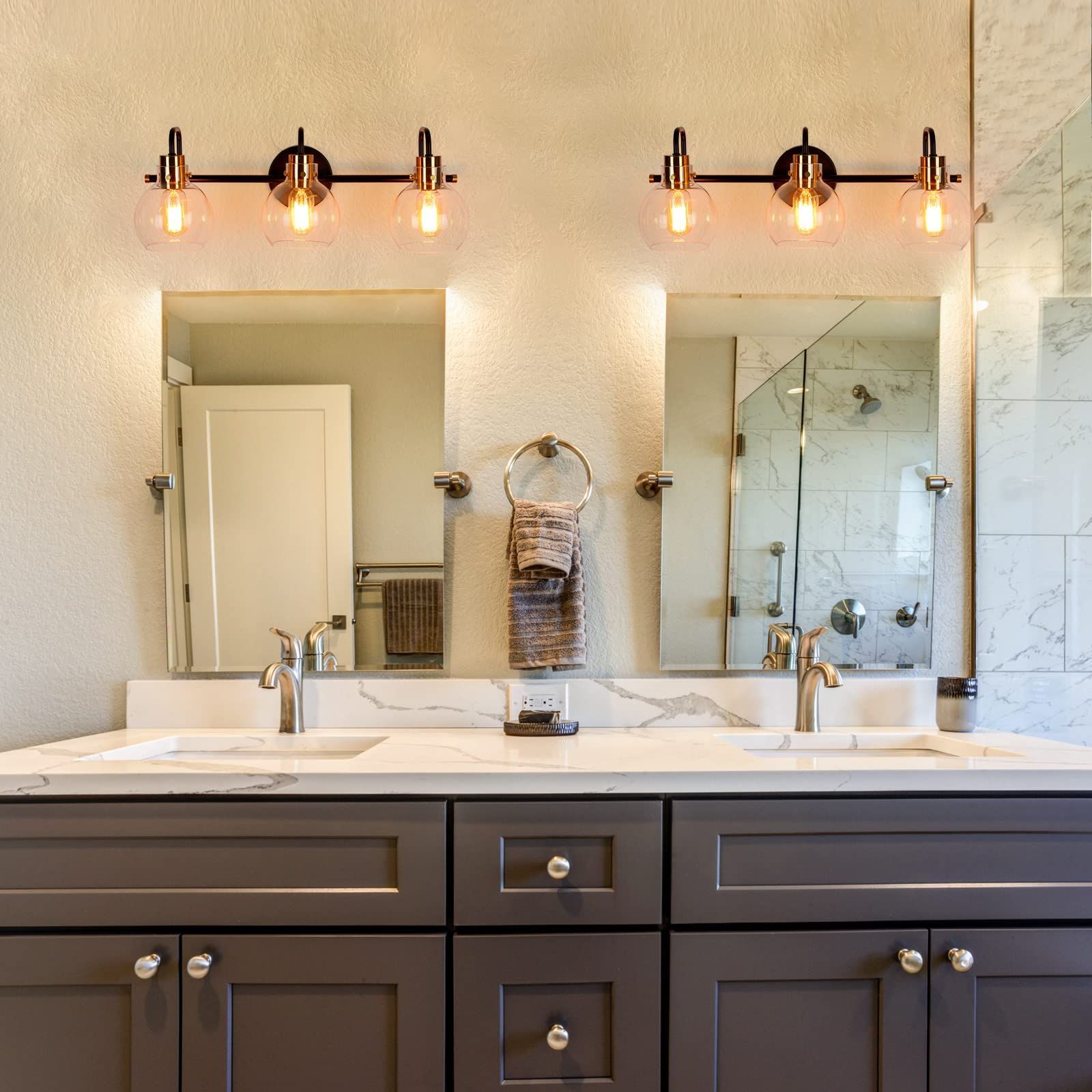 A bathroom vanity featuring a dark gray cabinet, two mirrors, dual sinks, and matching three-light brass wall fixtures.