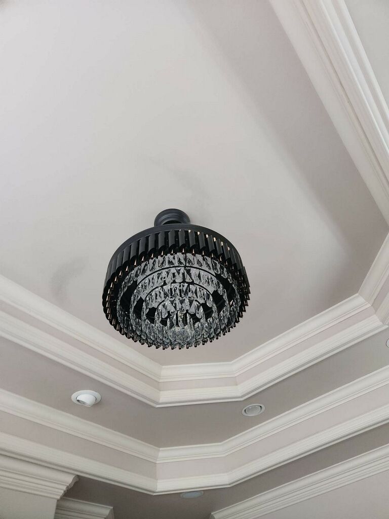 Chandelier hanging from a white ceiling with decorative molding, round with crystal accents.