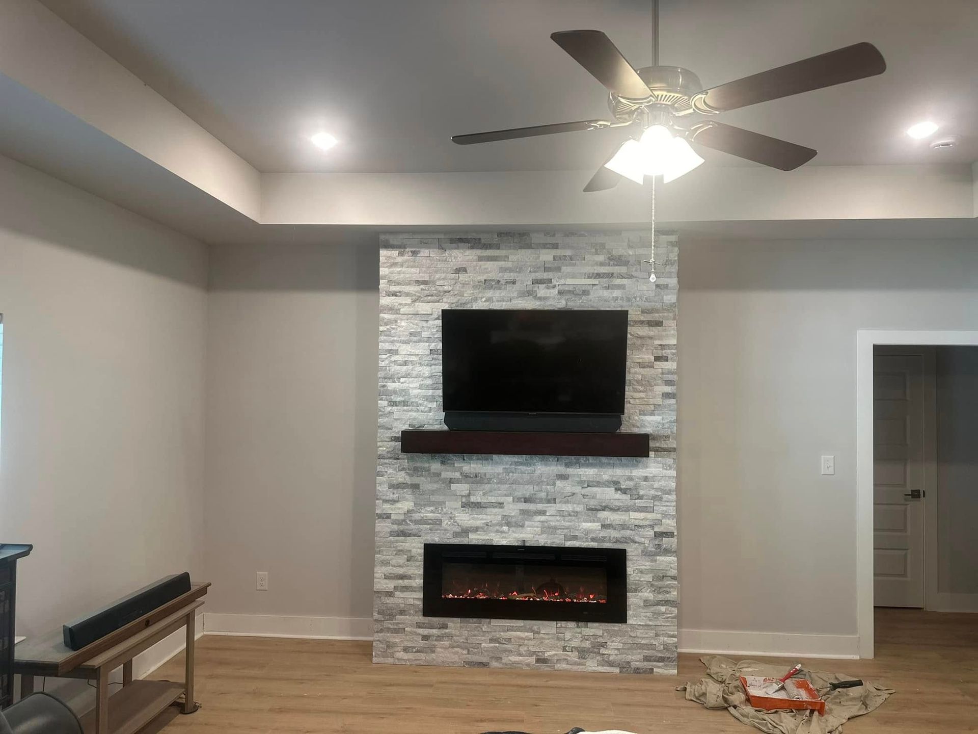Living room with a mounted TV over an electric fireplace, surrounded by light gray stacked stone, and a ceiling fan.
