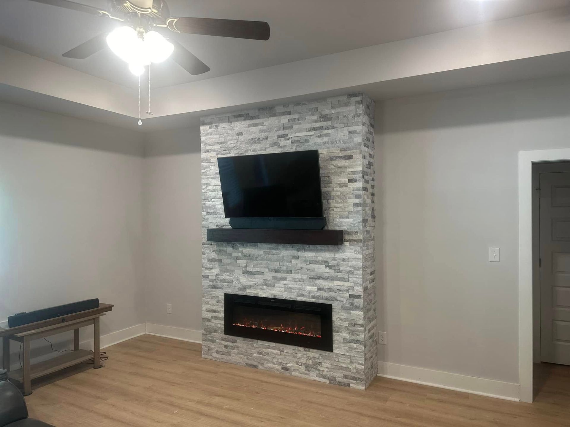 A living room features a stone-tiled fireplace wall with a built-in electric fireplace, a mounted TV, and a wood mantel.