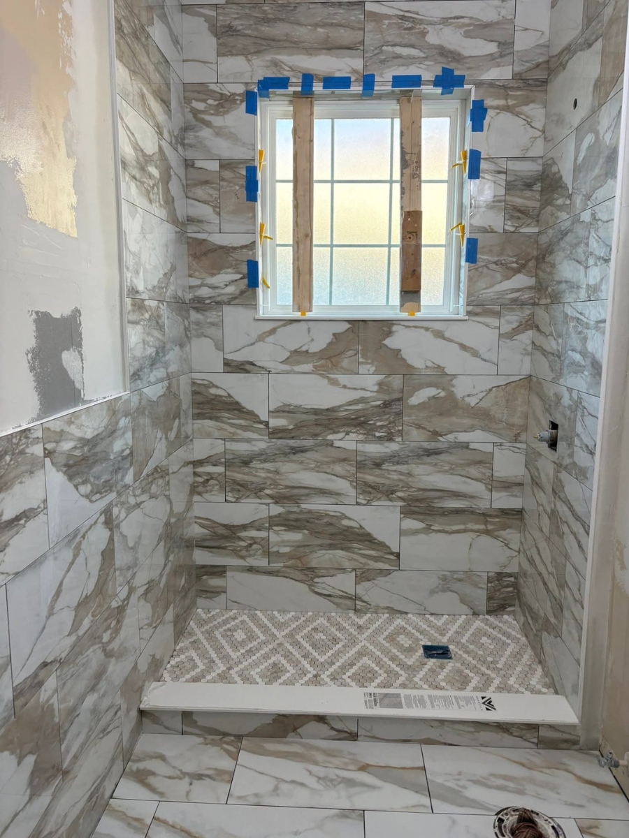 A shower under renovation, featuring large brown and white marbled wall tiles and patterned mosaic floor tiles.