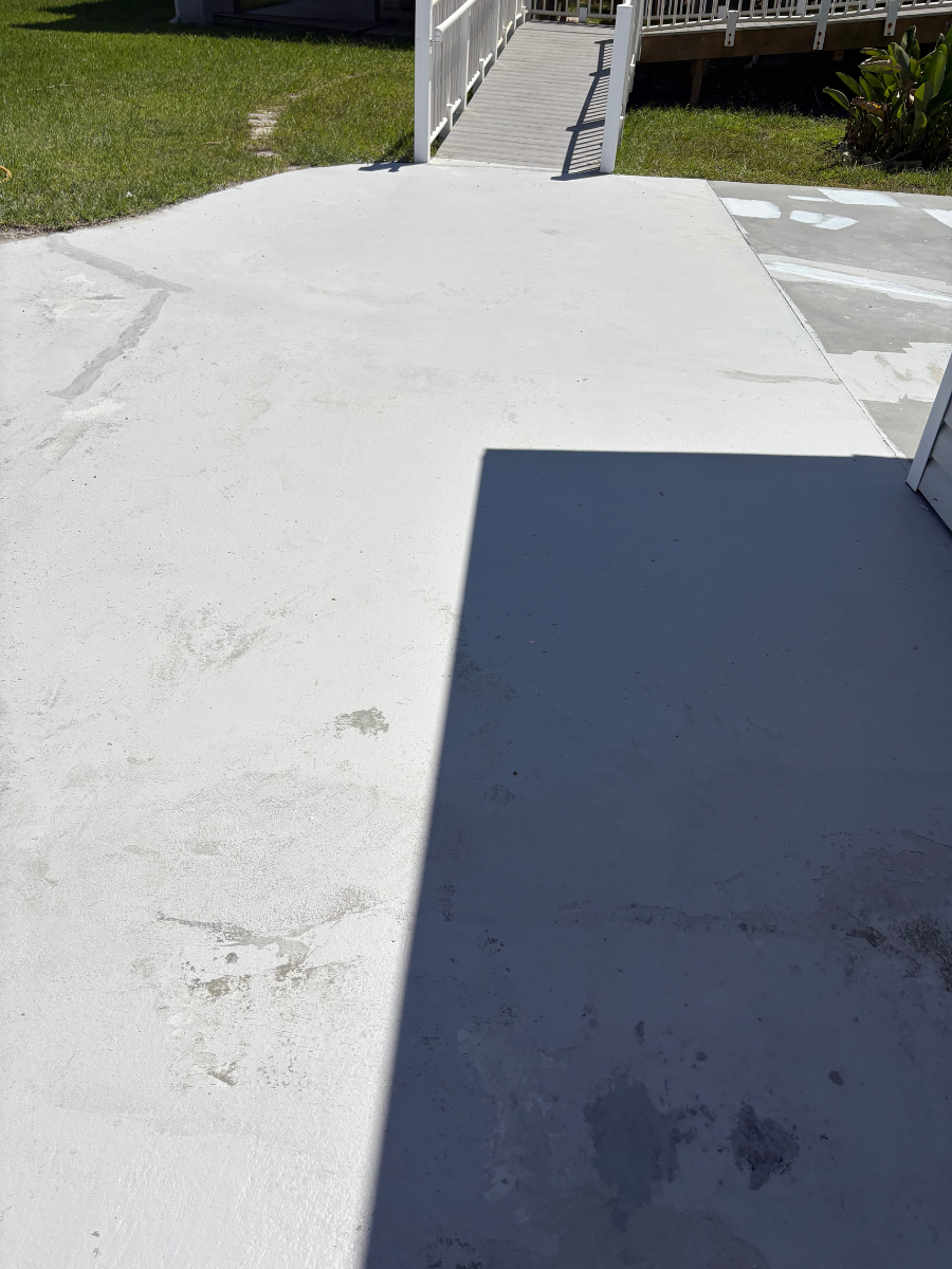 A light gray concrete patio with a sharp diagonal shadow, leading toward a white handrail and a ramp.