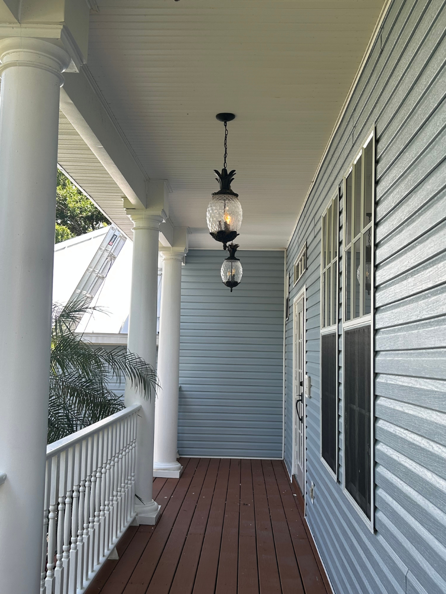 A porch with blue siding, white columns, wooden flooring, and two hanging lanterns.
