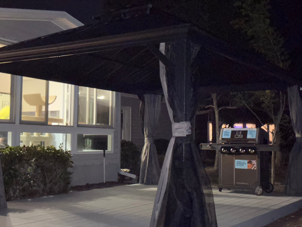 A black gazebo on a patio at night with a grill positioned underneath and a house visible in the background.
