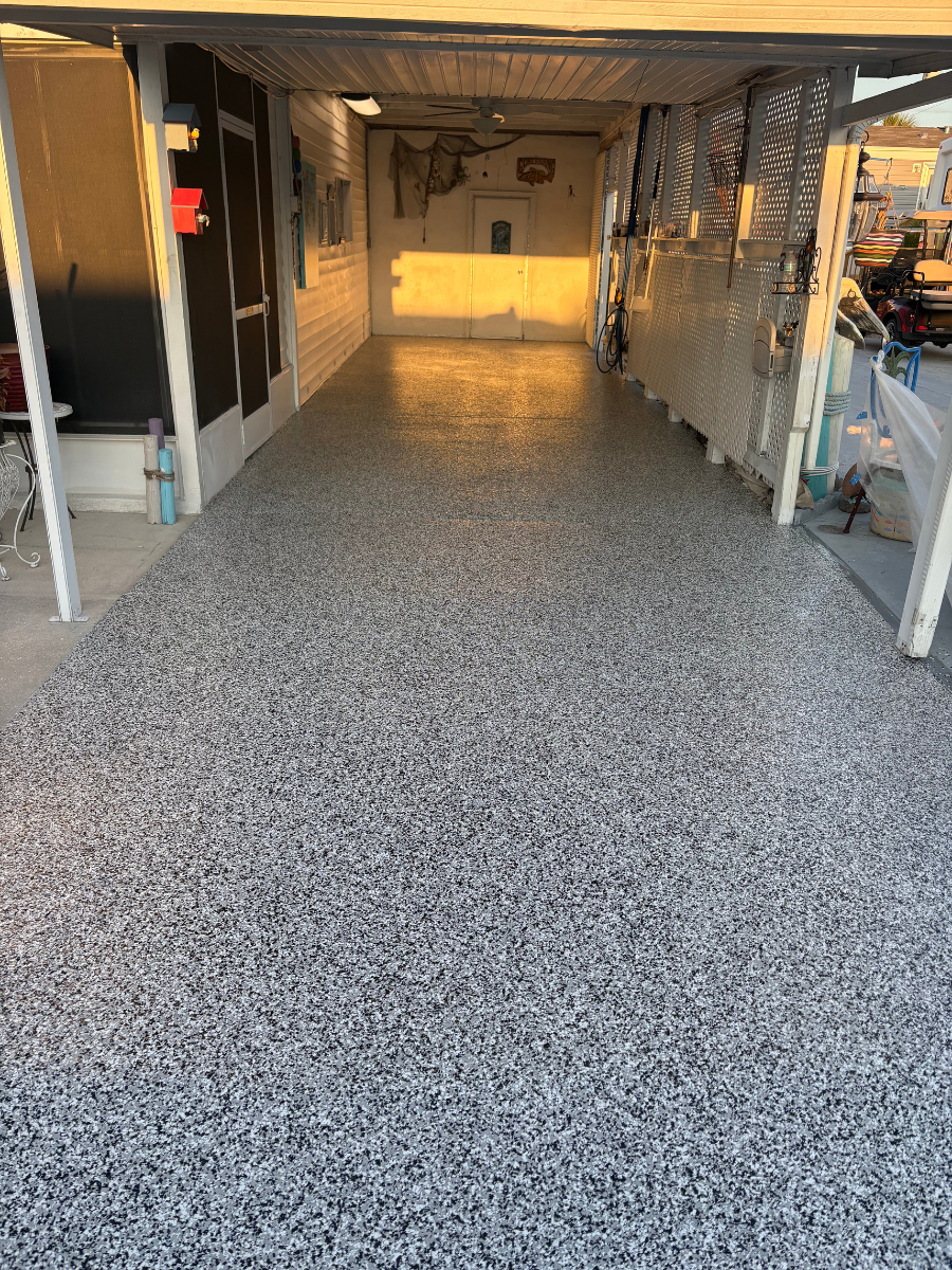 A covered outdoor patio or carport with a glossy, light grey and black speckled epoxy floor, bathed in warm golden light.