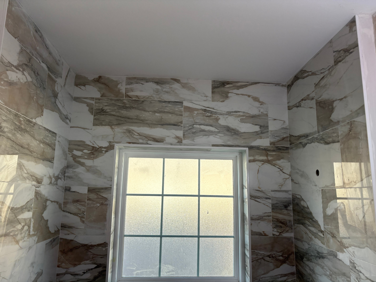 A square-grid window centered on a wall covered in large, white-and-brown marble-patterned ceramic tiles.