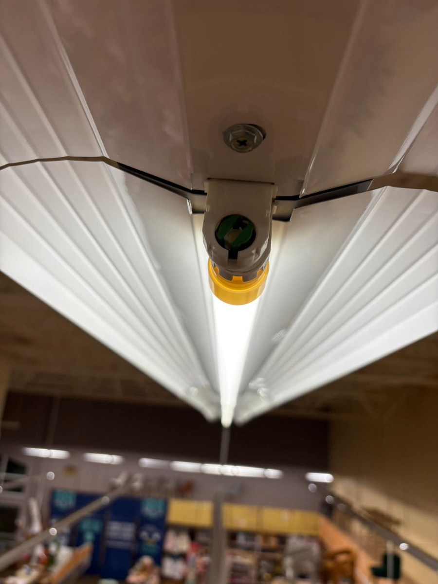 A close-up of a bright, linear LED light fixture mounted on a ceiling, showing the white casing and a yellow end cap.