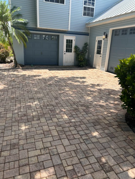 A paved stone driveway leads to a multi-story house featuring blue siding, two garage doors, and a white entry door.