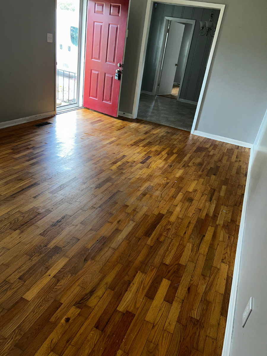 An indoor view of a room with polished wooden floors, a bright red front door, and an open doorway to another room.