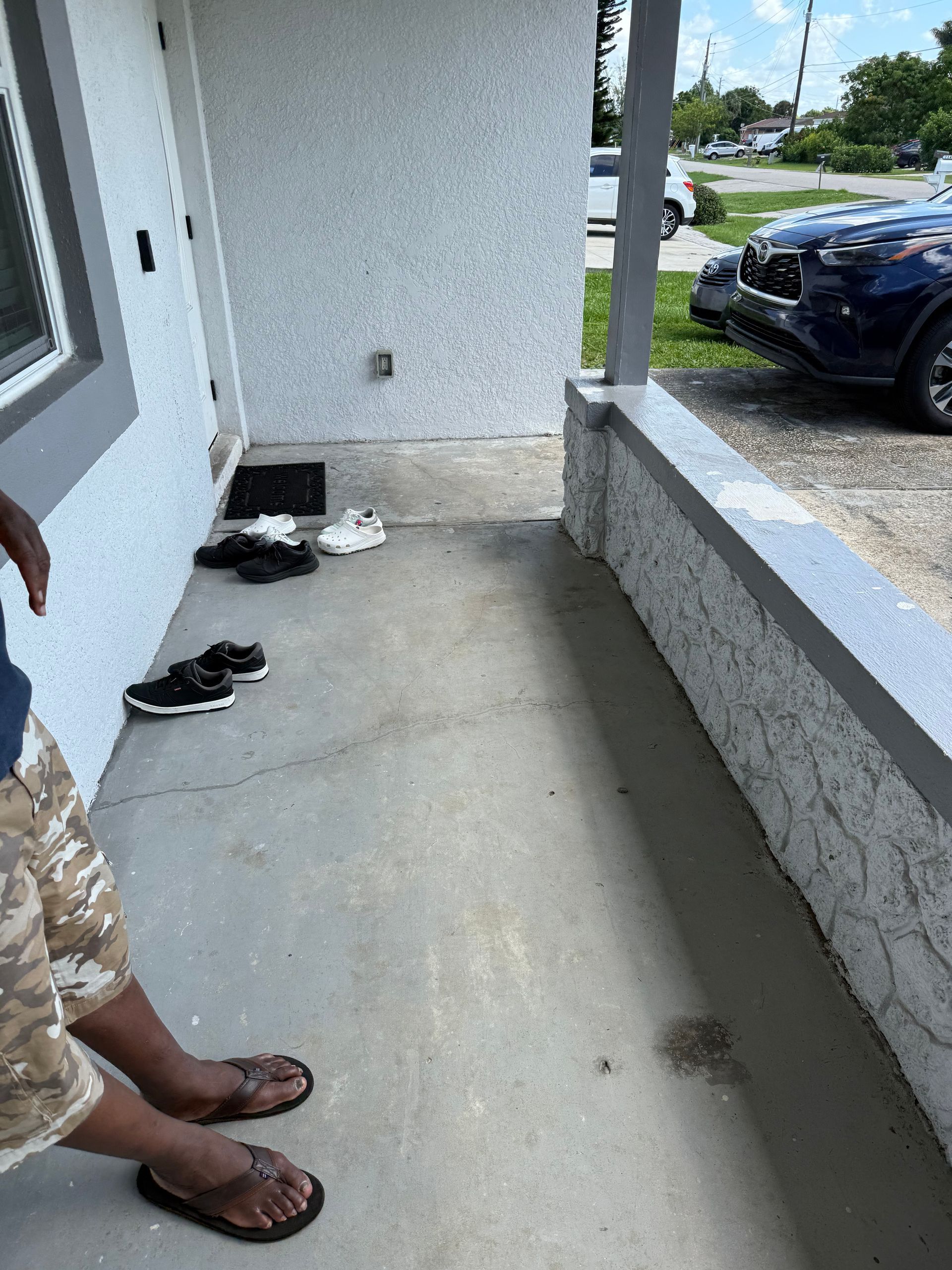 A porch area with several pairs of shoes near the doorway, viewed from the perspective of a person standing on the porch.
