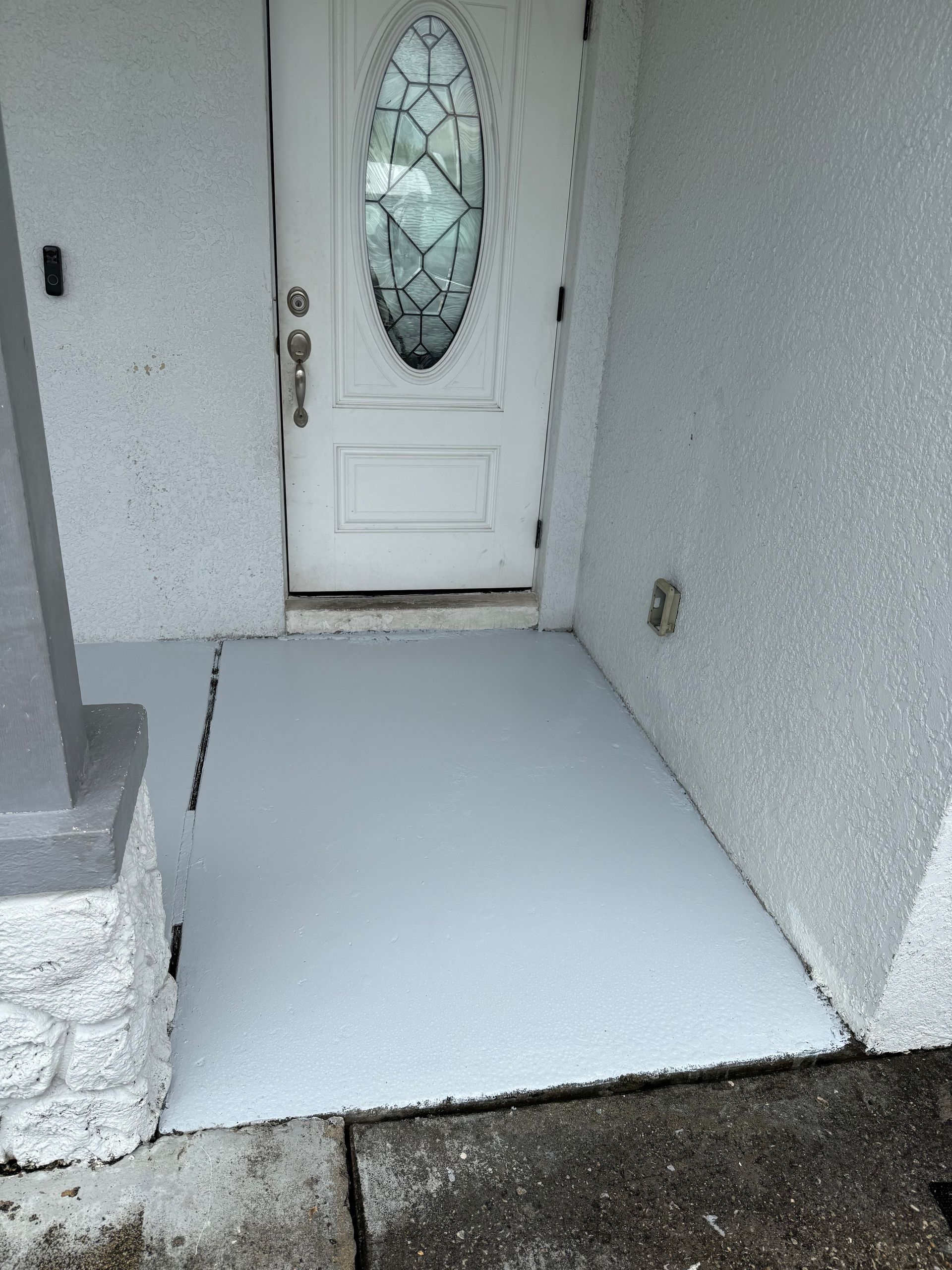 A white front door with an oval glass window, set above a freshly painted light gray concrete porch.