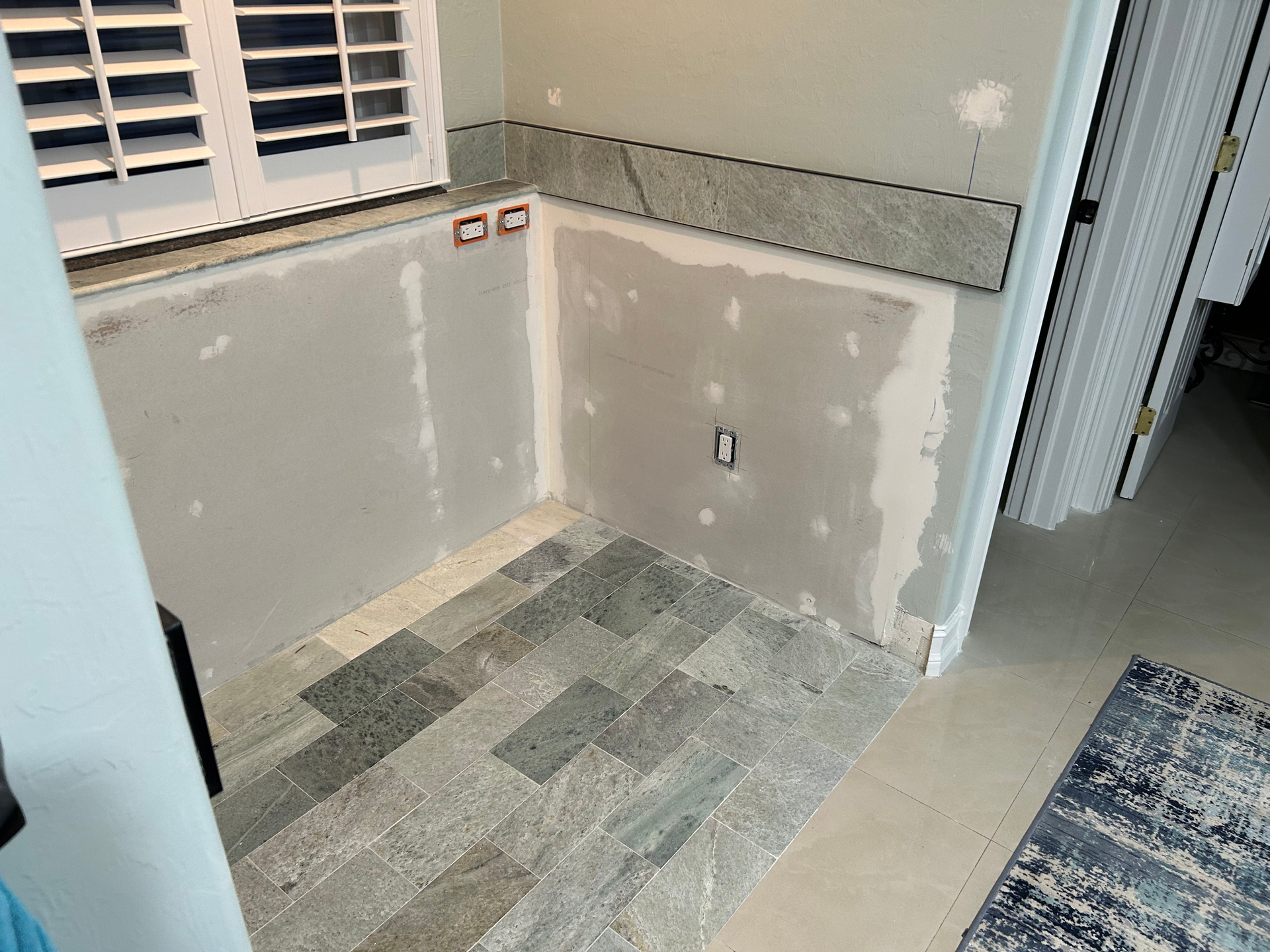 An interior corner featuring gray, unfinished drywall walls with stone flooring and a matching stone border backsplash.
