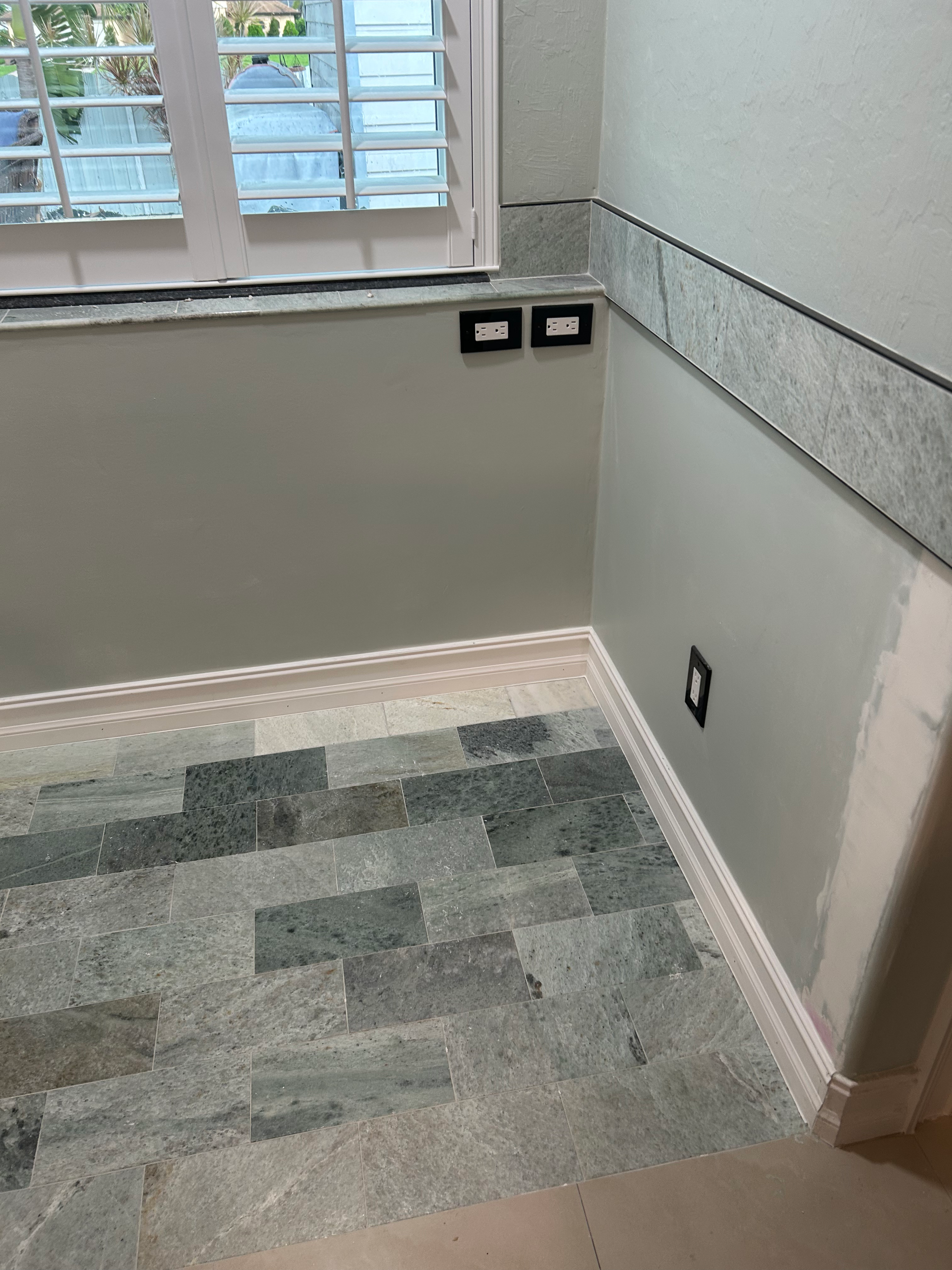 A corner room featuring light gray walls, a stone tile floor, and a matching stone backsplash with two light switches.