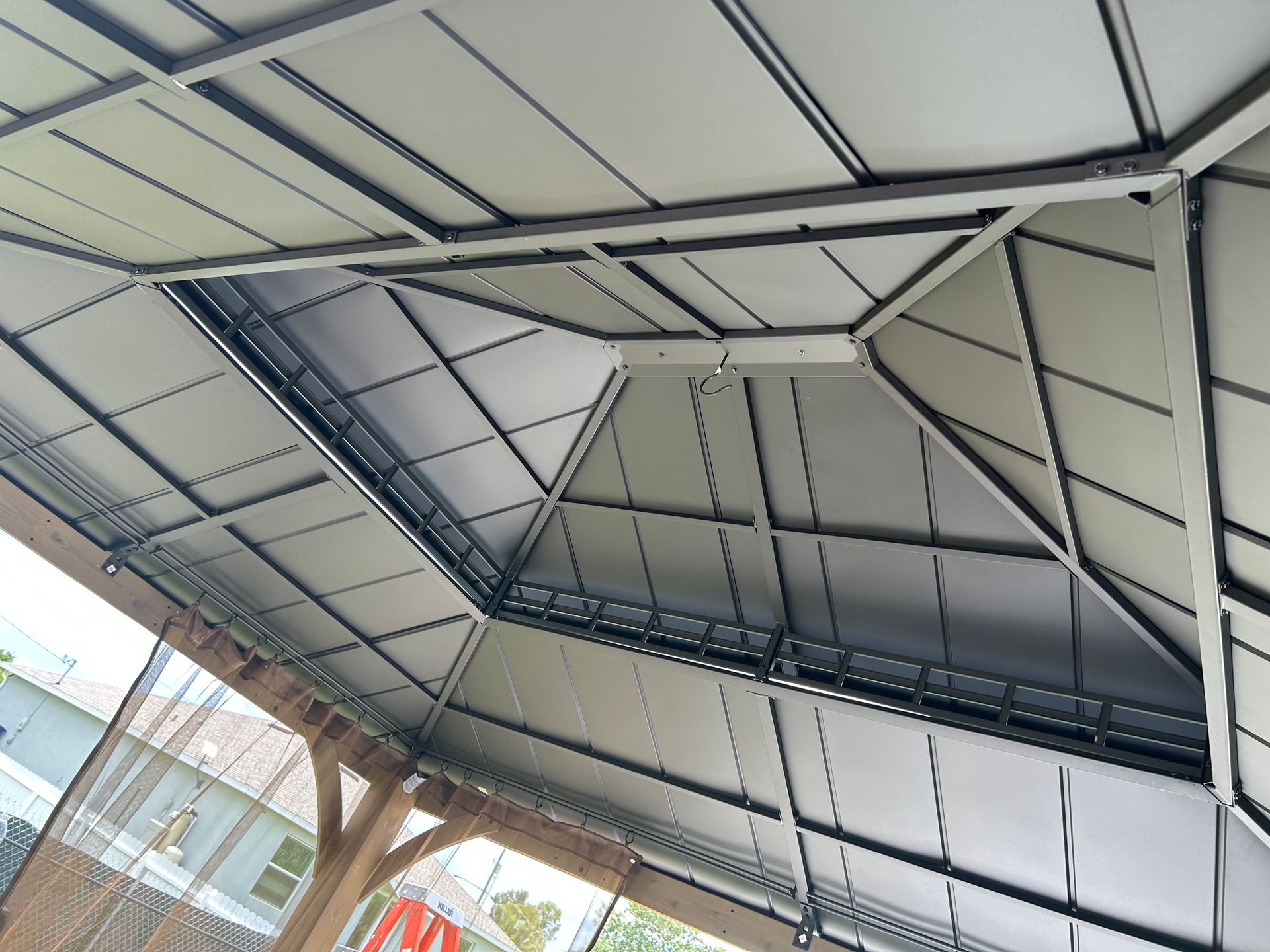 An angled view of the underside of a metal gazebo roof featuring a tiered, paneled design with dark structural beams.