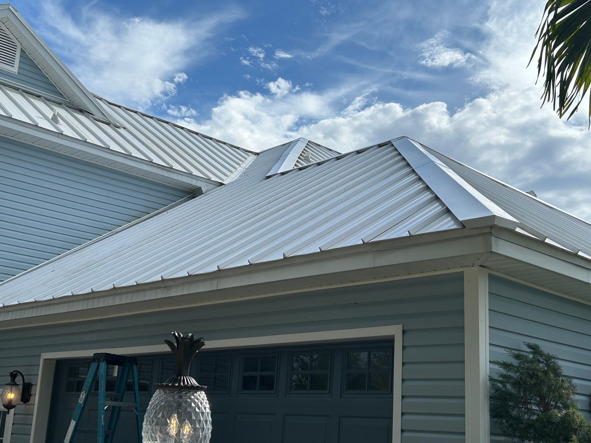 Light blue house with a white metal roof under a bright, partly cloudy sky.