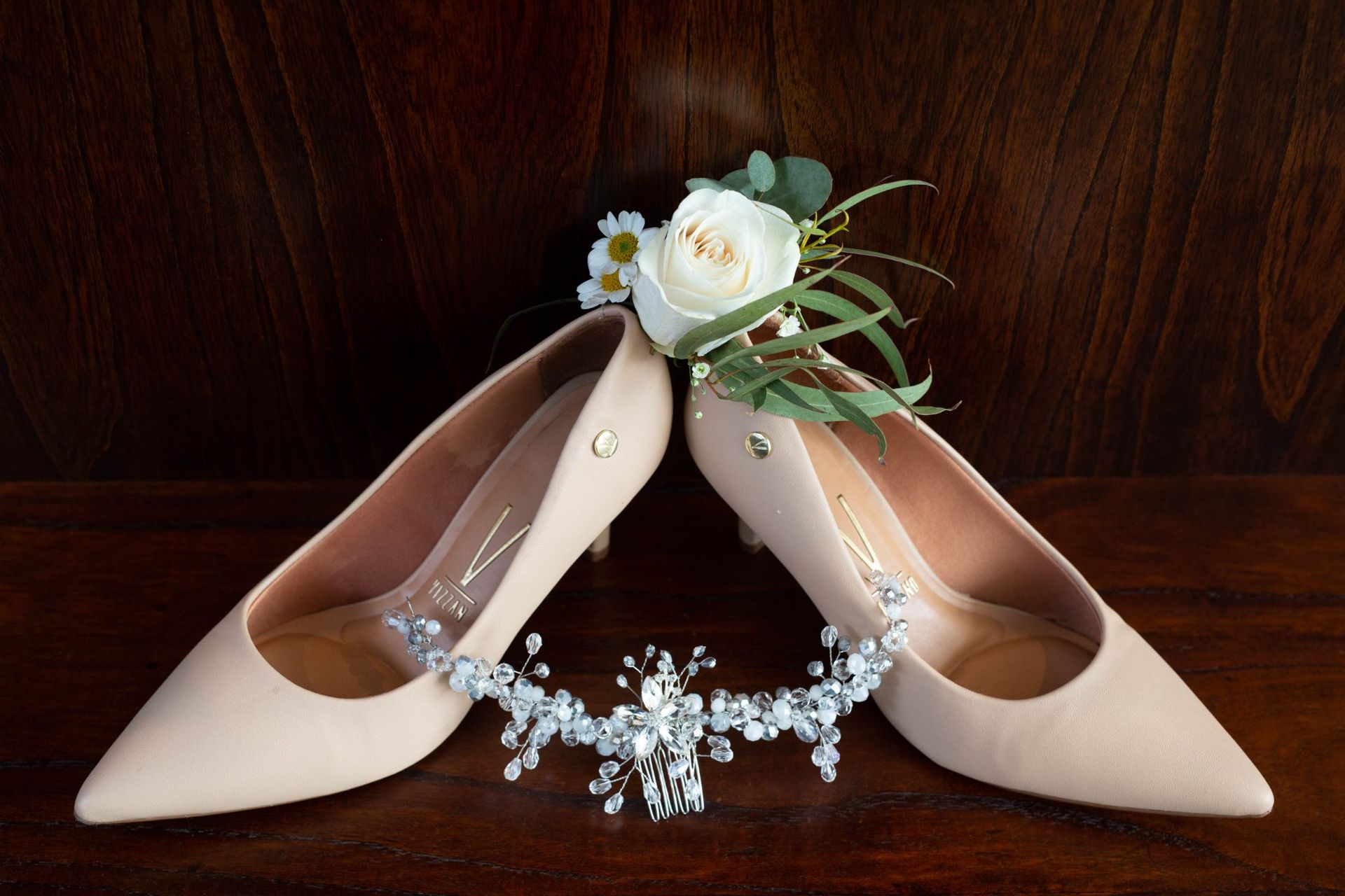 Zapatos de novia de color rubor con detalles florales y un tocado brillante sobre una superficie de madera oscura.