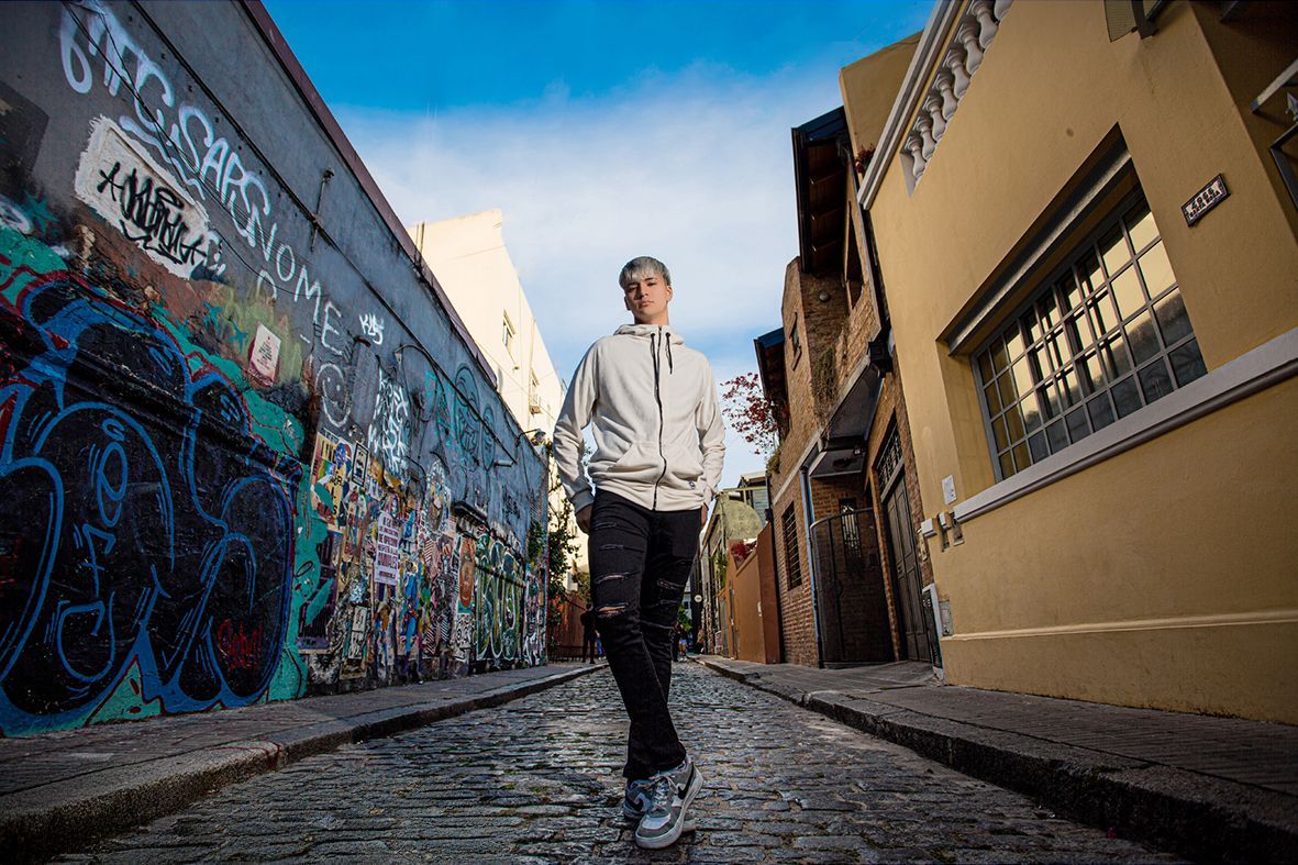 Hombre caminando hacia la cámara en un callejón estrecho con grafitis en una pared.