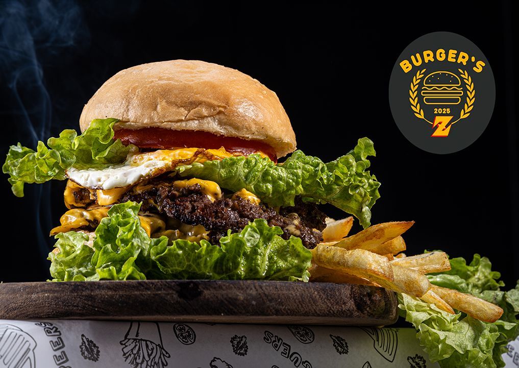 Hamburguesa grande con lechuga, queso, huevo frito y papas fritas sobre una tabla de madera.