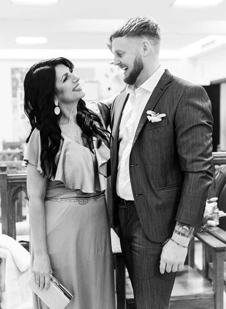 Mujer vestida y hombre de traje sonriendo y abrazándose en un edificio.