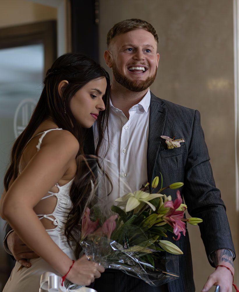Los recién casados se abrazan; la novia sostiene el ramo. El hombre sonríe, vestido de traje.