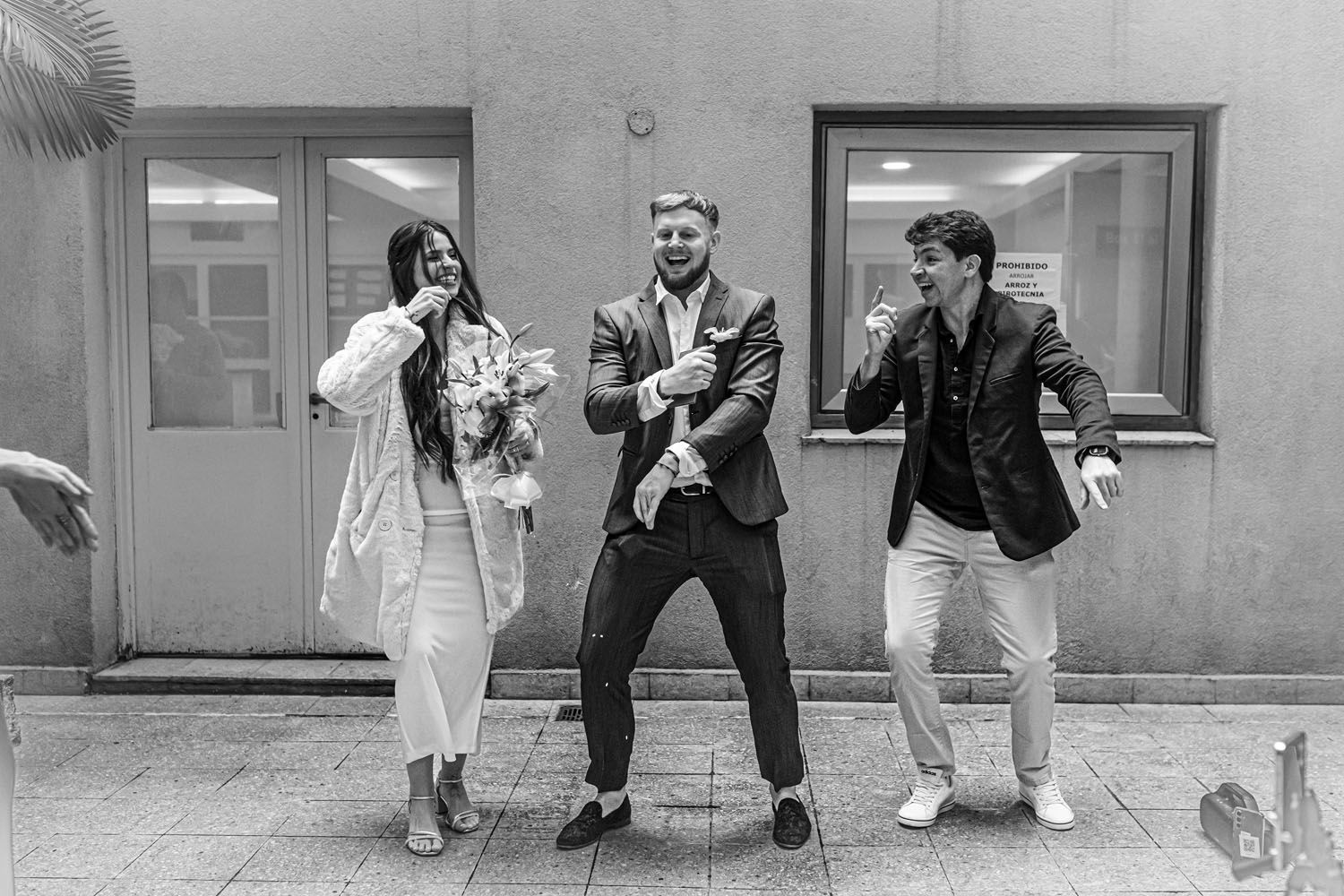 Tres personas bailan alegremente frente a un edificio. Vestían ropa formal.