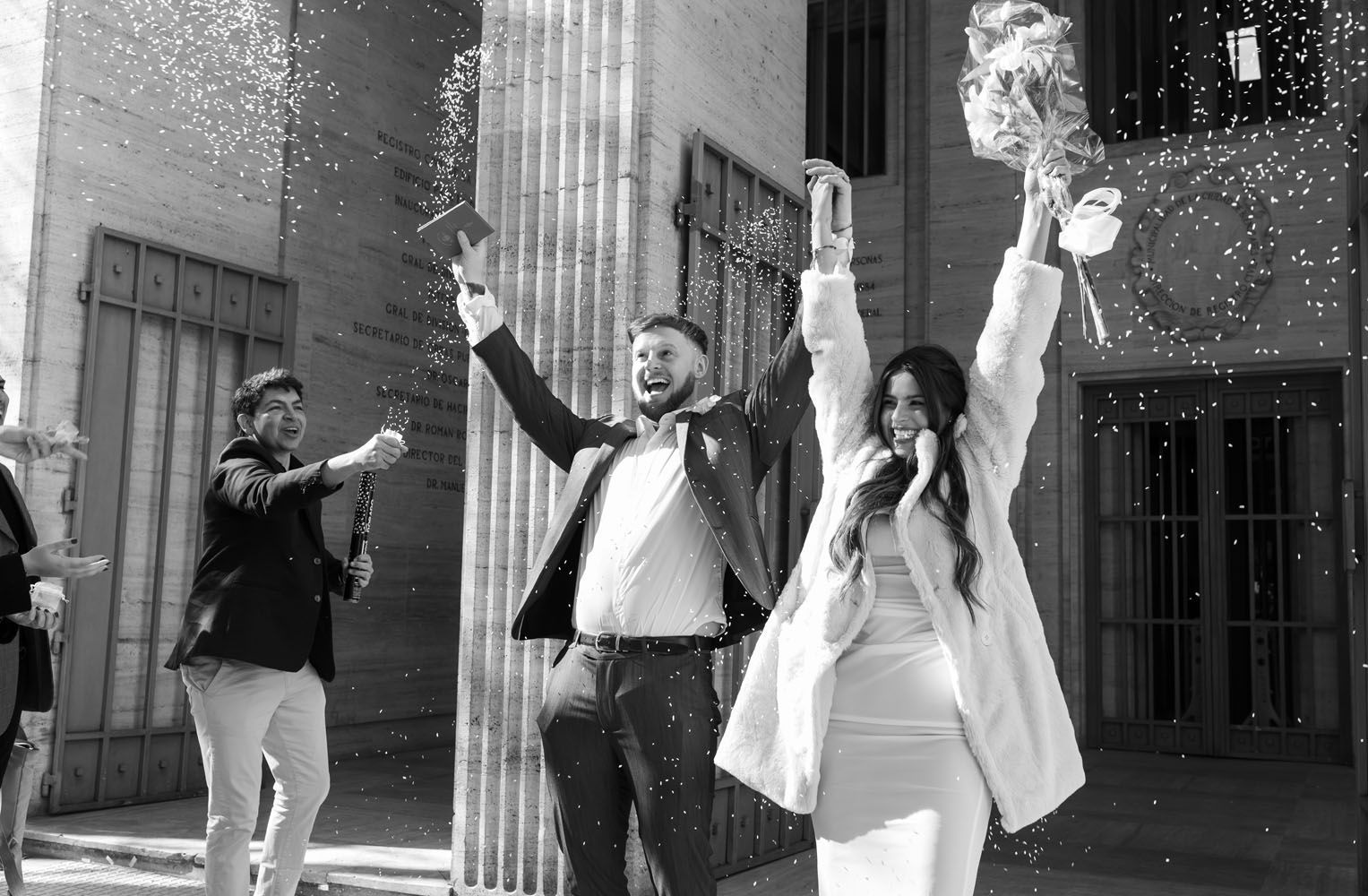 Una pareja celebra su boda con confeti, con los brazos en alto. El hombre a la izquierda activa el cañón de confeti.