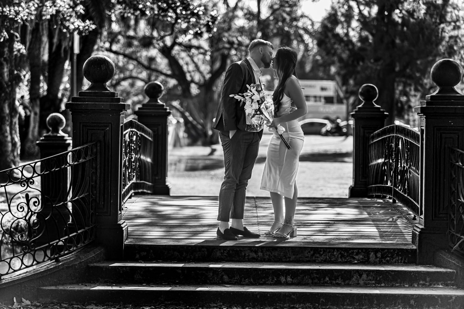 Pareja besándose en un puente decorativo en un parque. Foto en blanco y negro.
