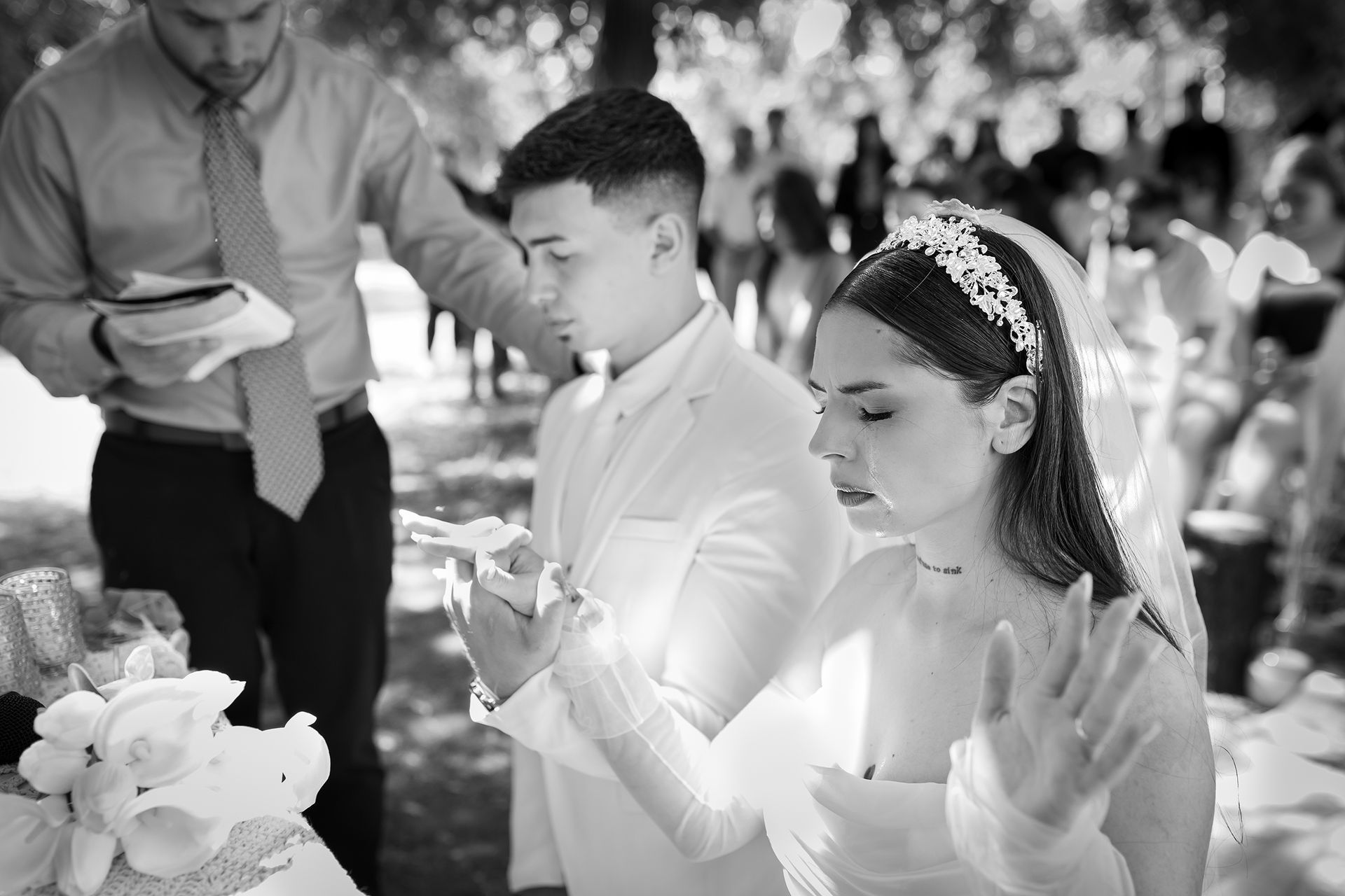Ceremonia de boda: Pareja encendiendo velas al aire libre; el oficiante sostiene los materiales; invitados en el fondo.
