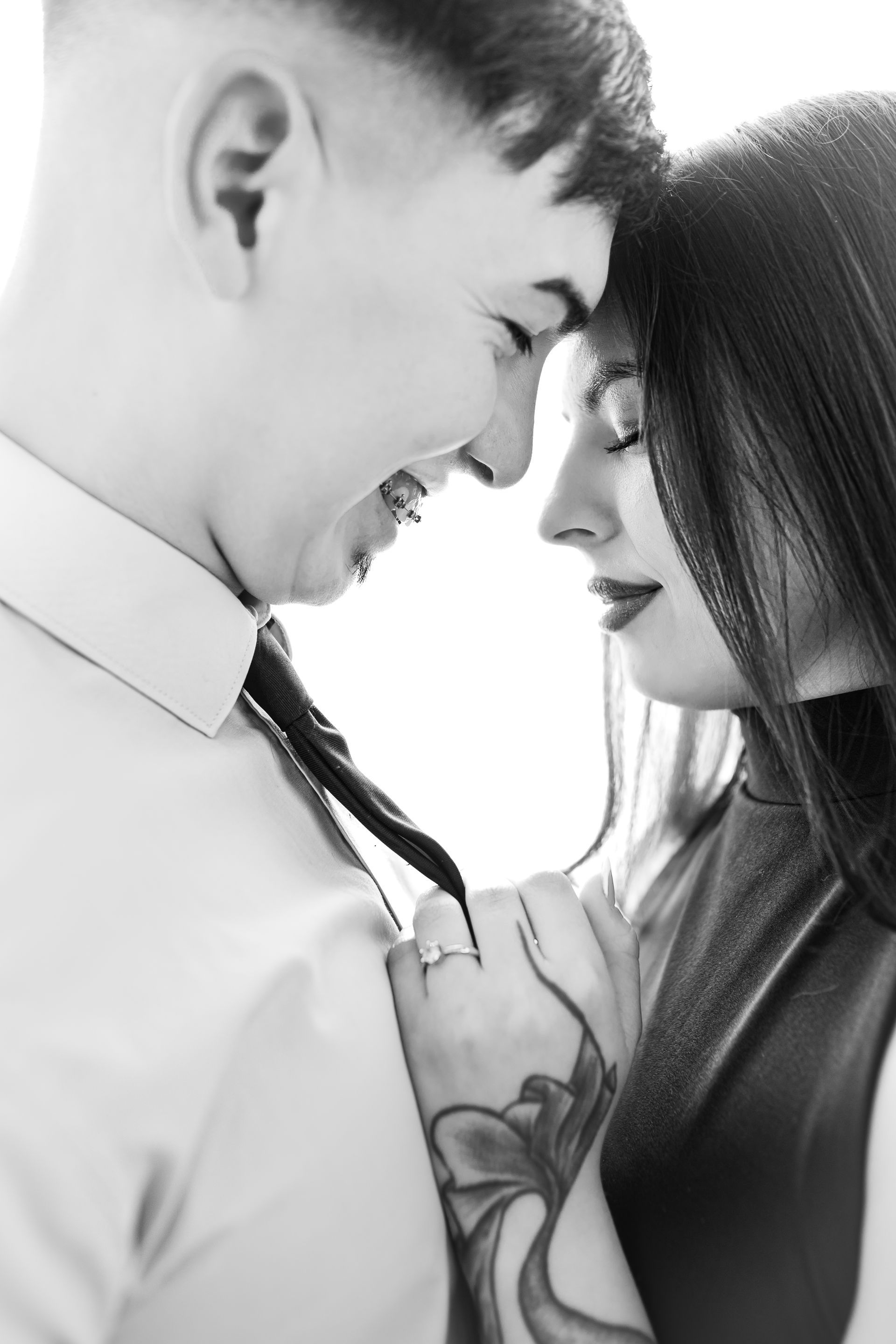 Pareja abrazándose; hombre tirando de la corbata de la mujer, ambos sonriendo, foto en blanco y negro.