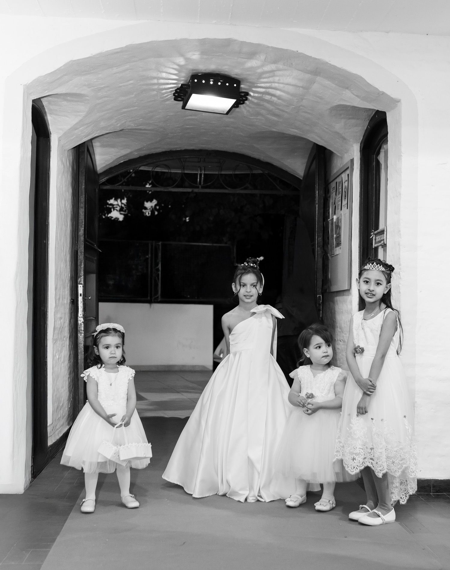 Cuatro muchachas jóvenes con vestidos formales se encuentran en una puerta arqueada.