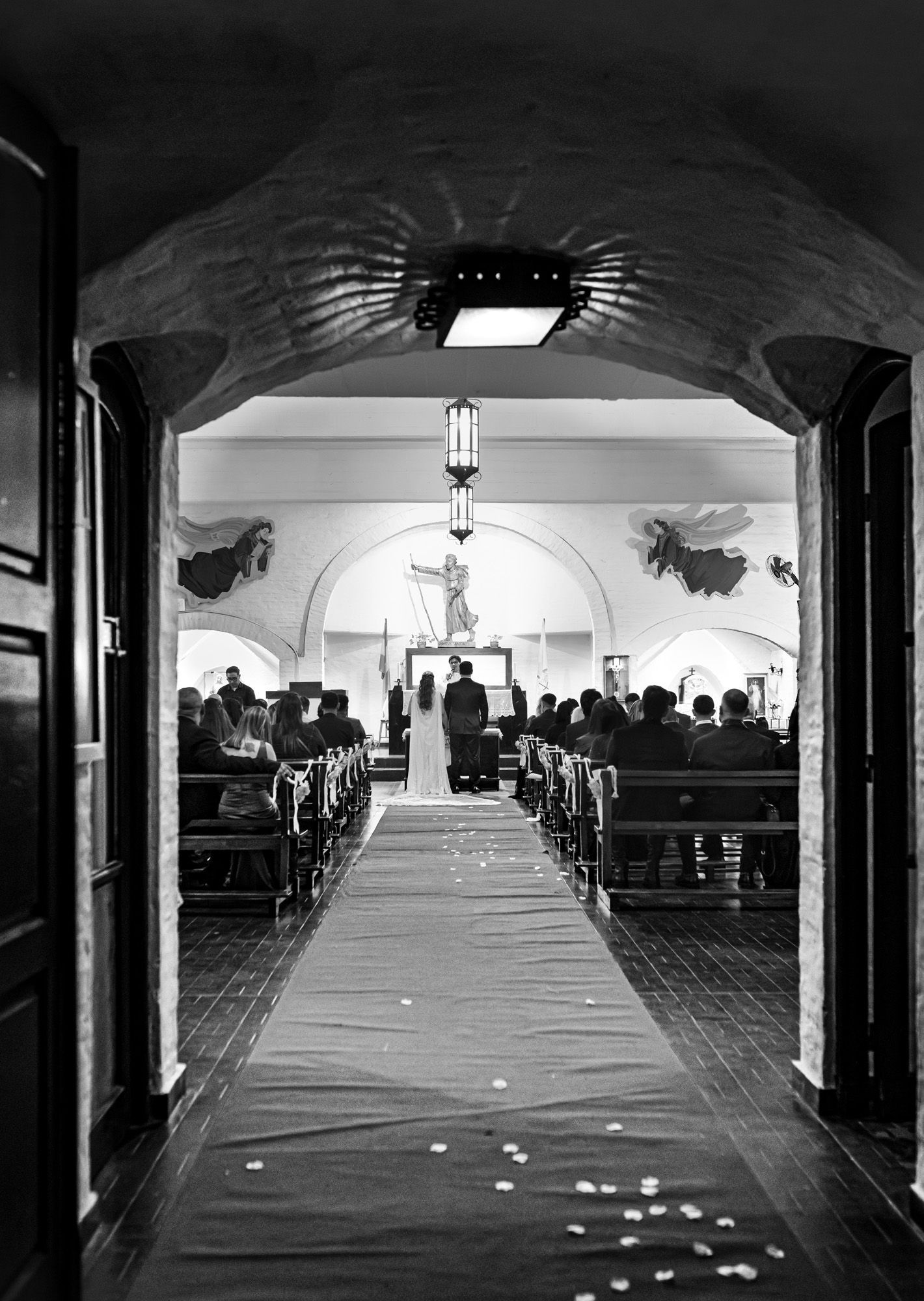 Ceremonia de boda en una iglesia; pareja en el altar, invitados sentados, pasillo rojo y luz entrando por la puerta.