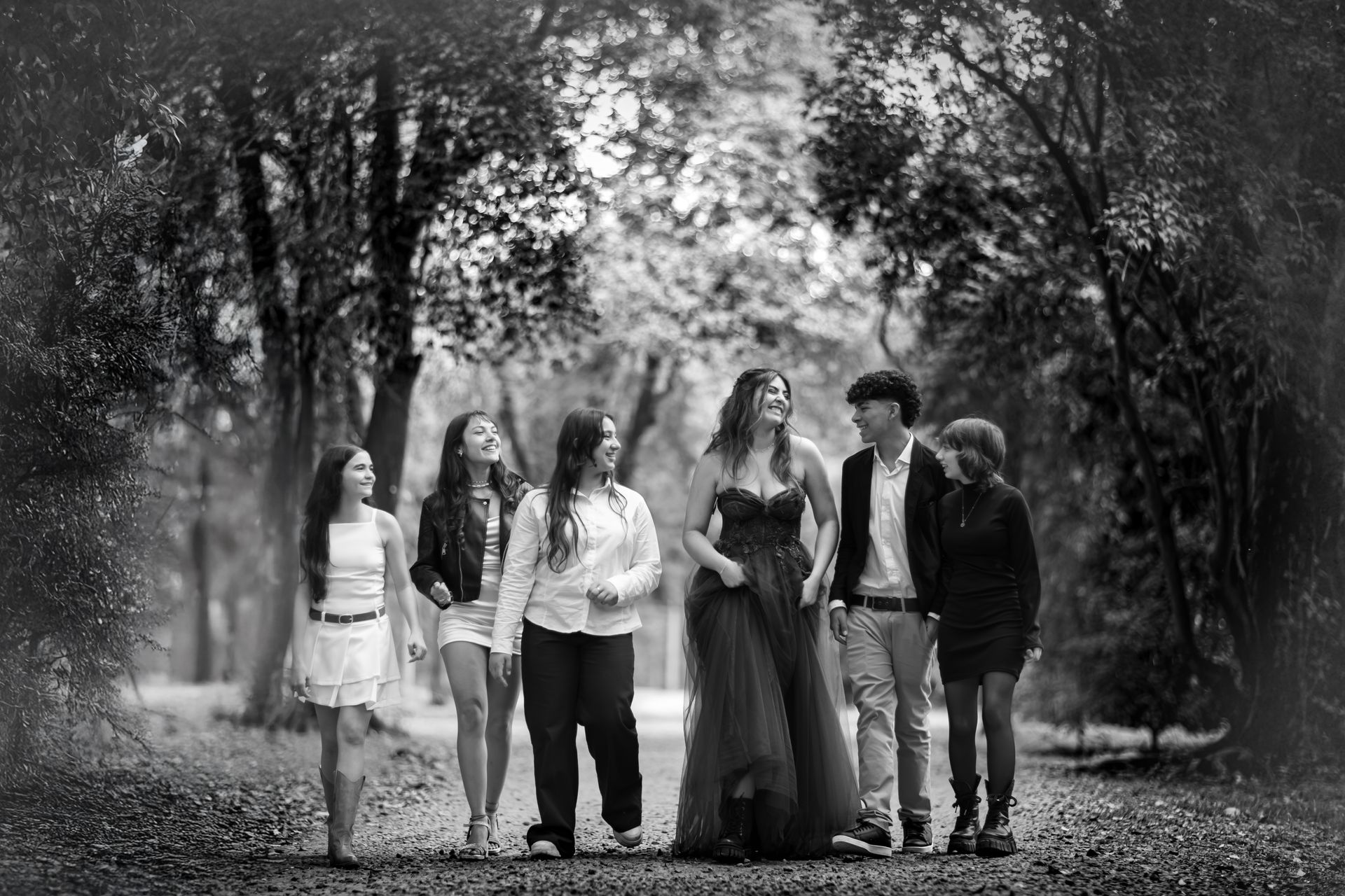 Grupo de personas caminando por un sendero en un parque, sonriendo, árboles de fondo, foto en blanco y negro.