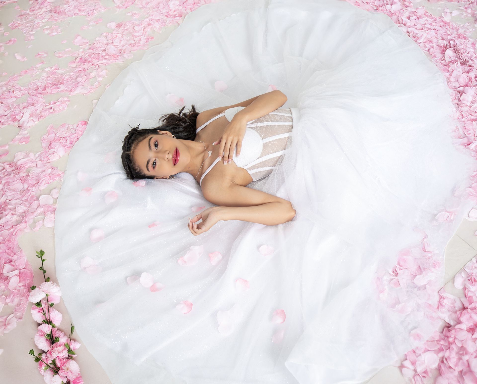 Una mujer con un vestido de novia blanco yace en un lecho de pétalos de flores rosas.