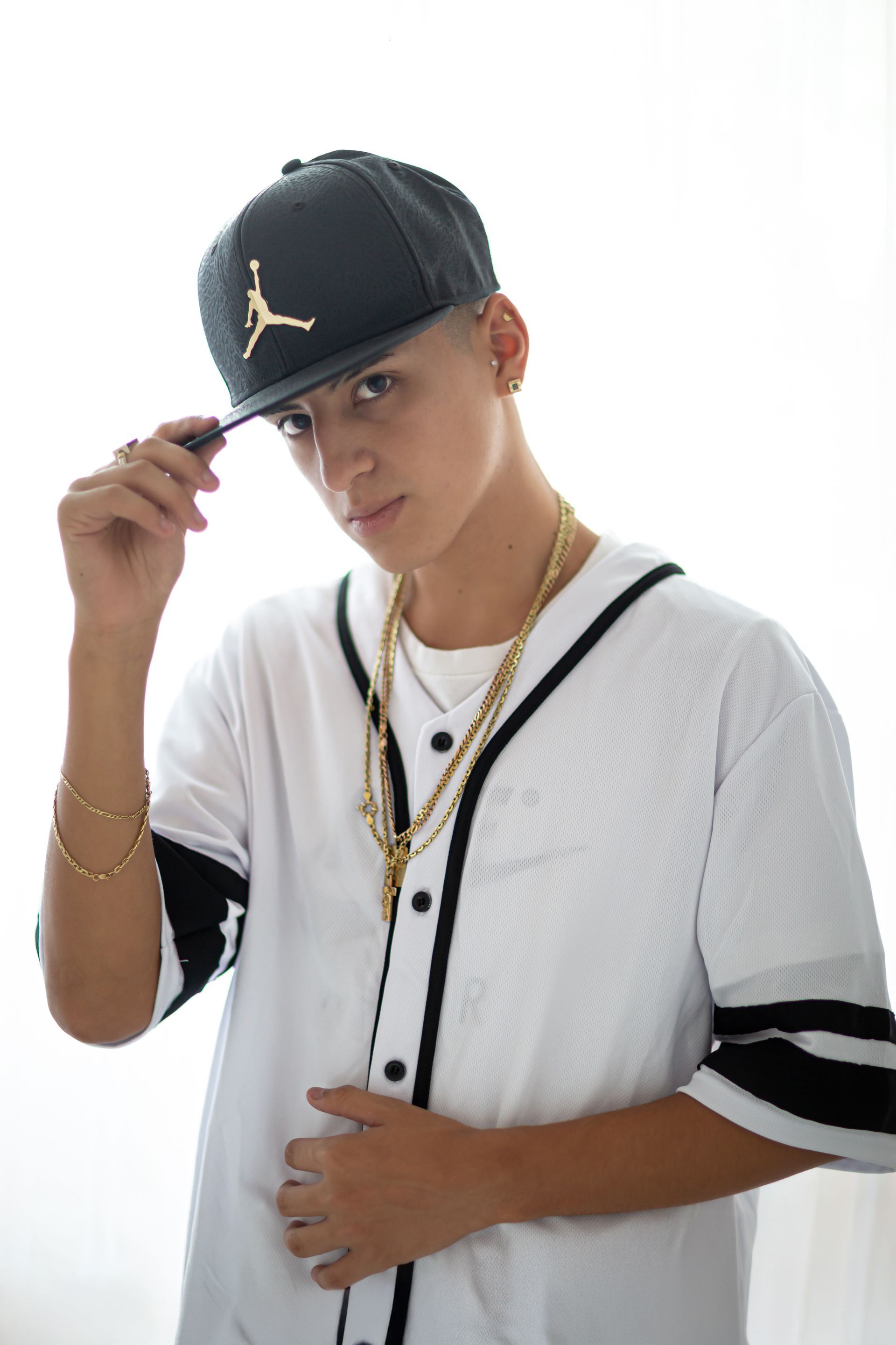 Persona con camiseta blanca y joyas de oro que lleva una gorra Jordan, tocando el ala.