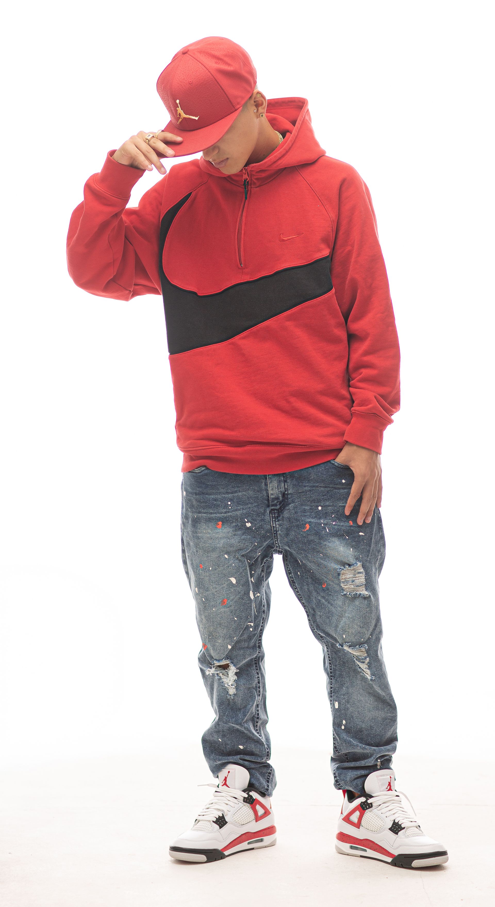 Persona con sudadera y gorra rojas, jeans desgastados y zapatillas deportivas, posando con la mano en la gorra.