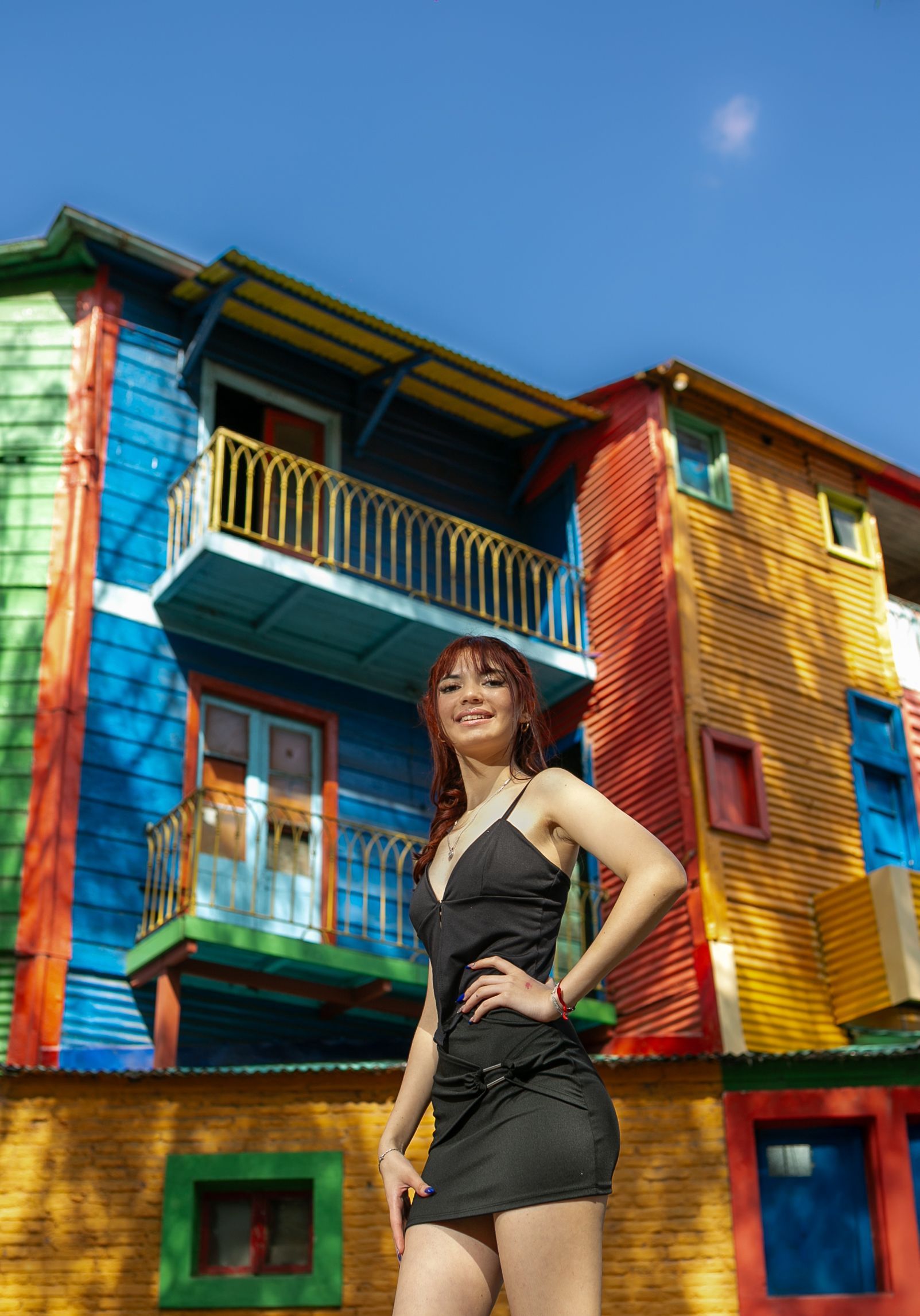 Mujer vestida de negro posa frente a edificios coloridos y pintados en La Boca, Buenos Aires.