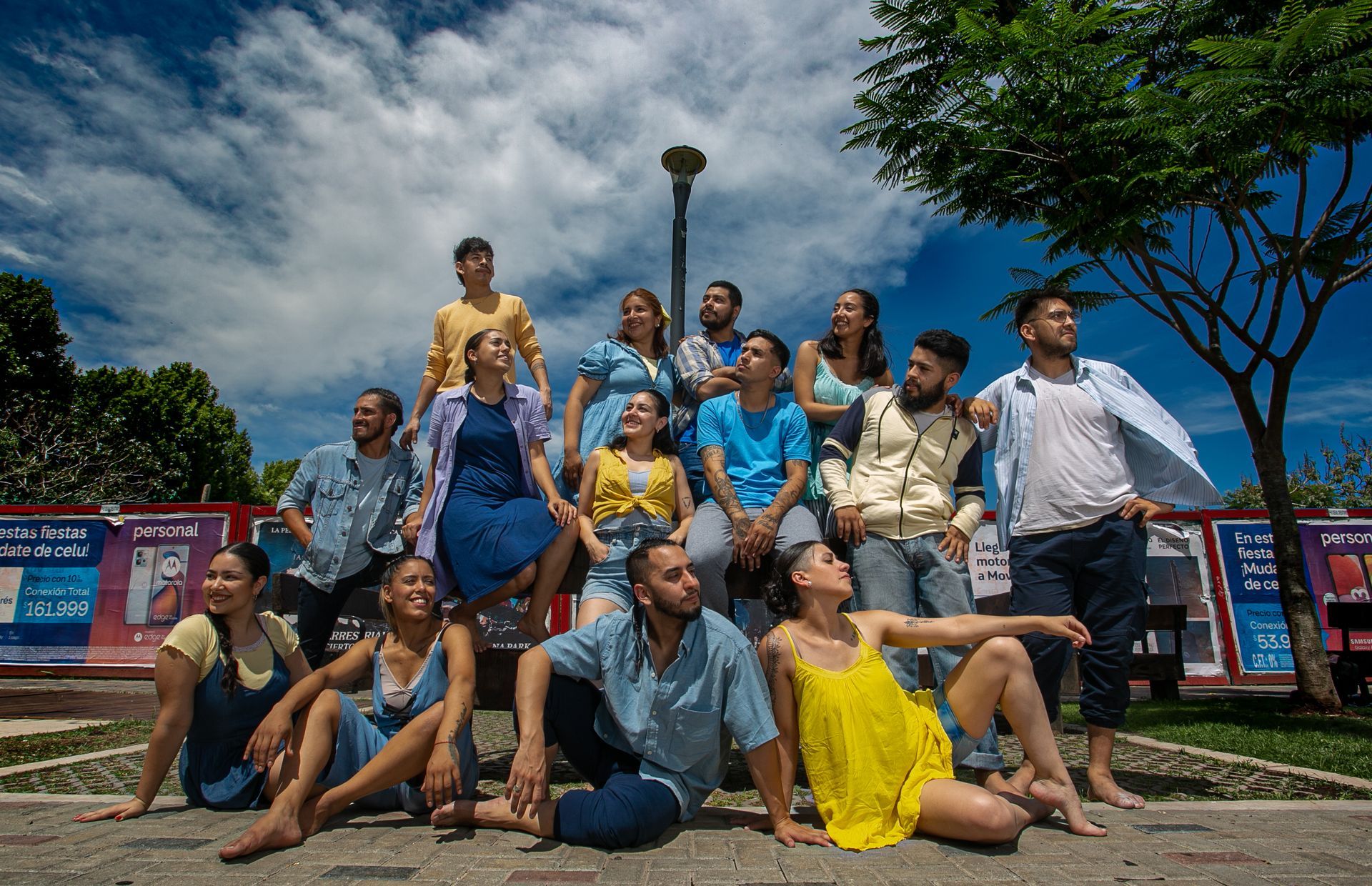 Grupo de personas posando al aire libre; cielo azul; ropa de varios colores; entorno de parque.