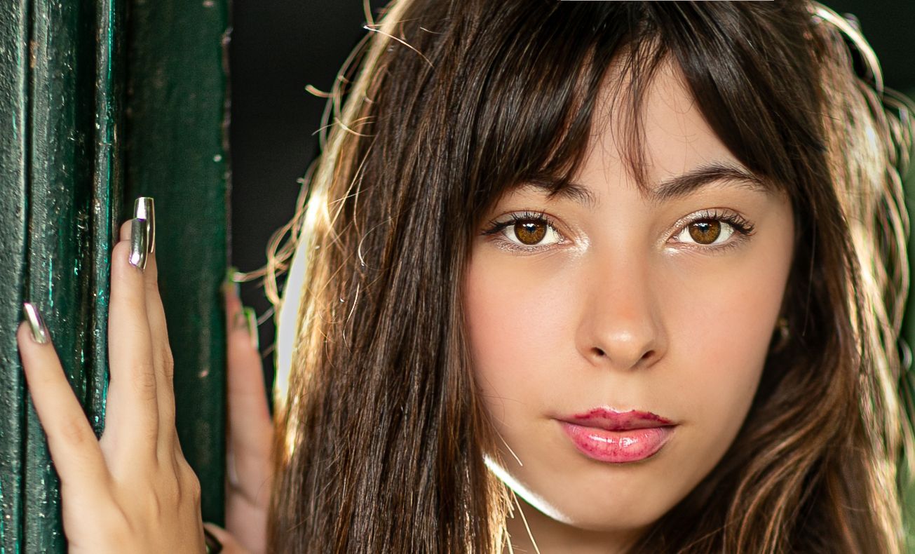 Mujer con cabello oscuro y flequillo, apoyando la mano sobre una estructura verde, mirando a la cámara.