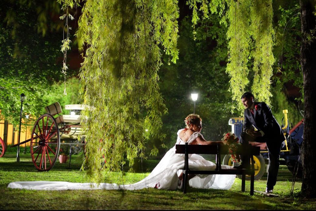 Los novios posan en un banco al aire libre por la noche. La novia lleva un vestido blanco y el novio un traje oscuro.