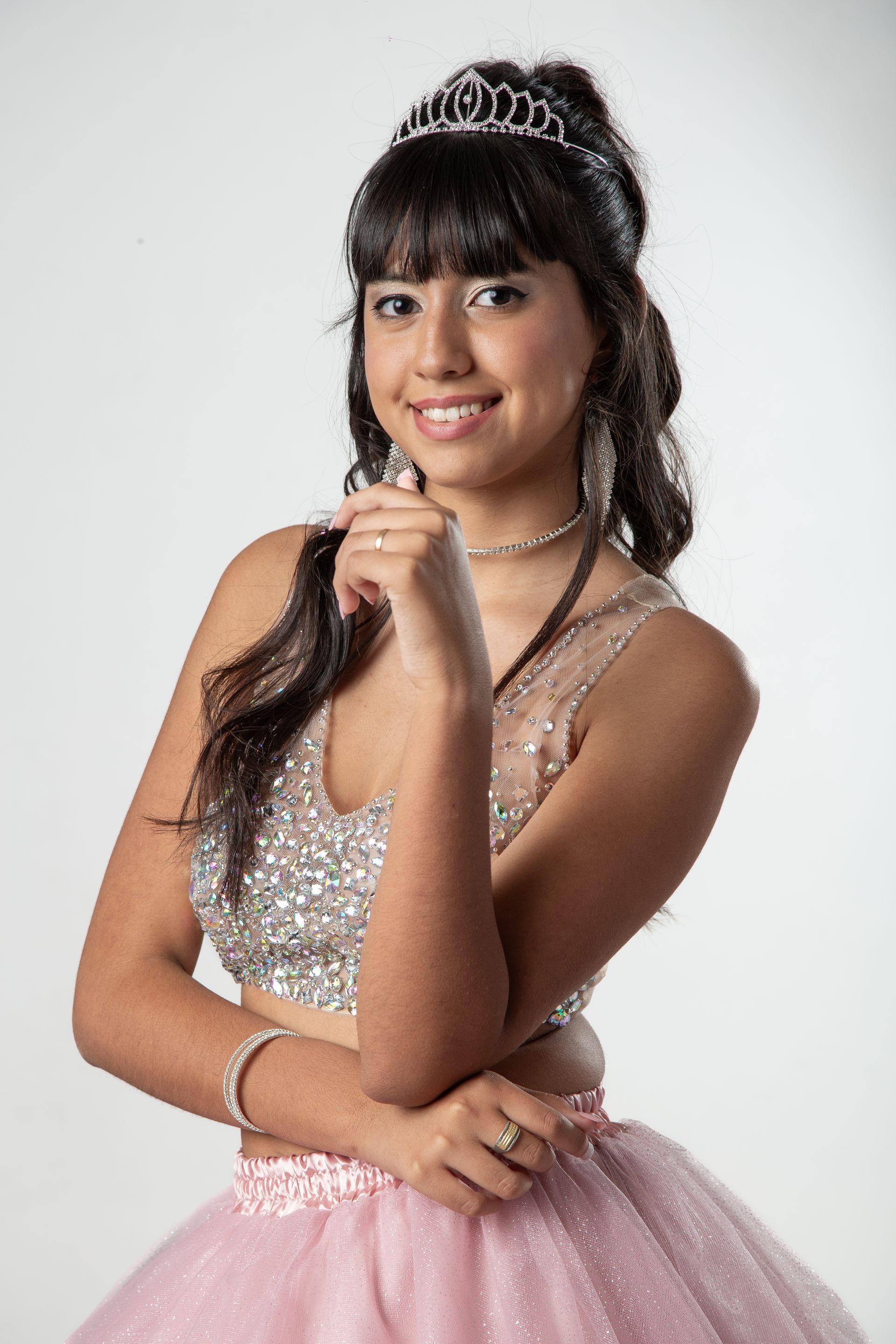 Mujer con tiara y vestido rosa brillante, sonriendo, posando en un estudio.