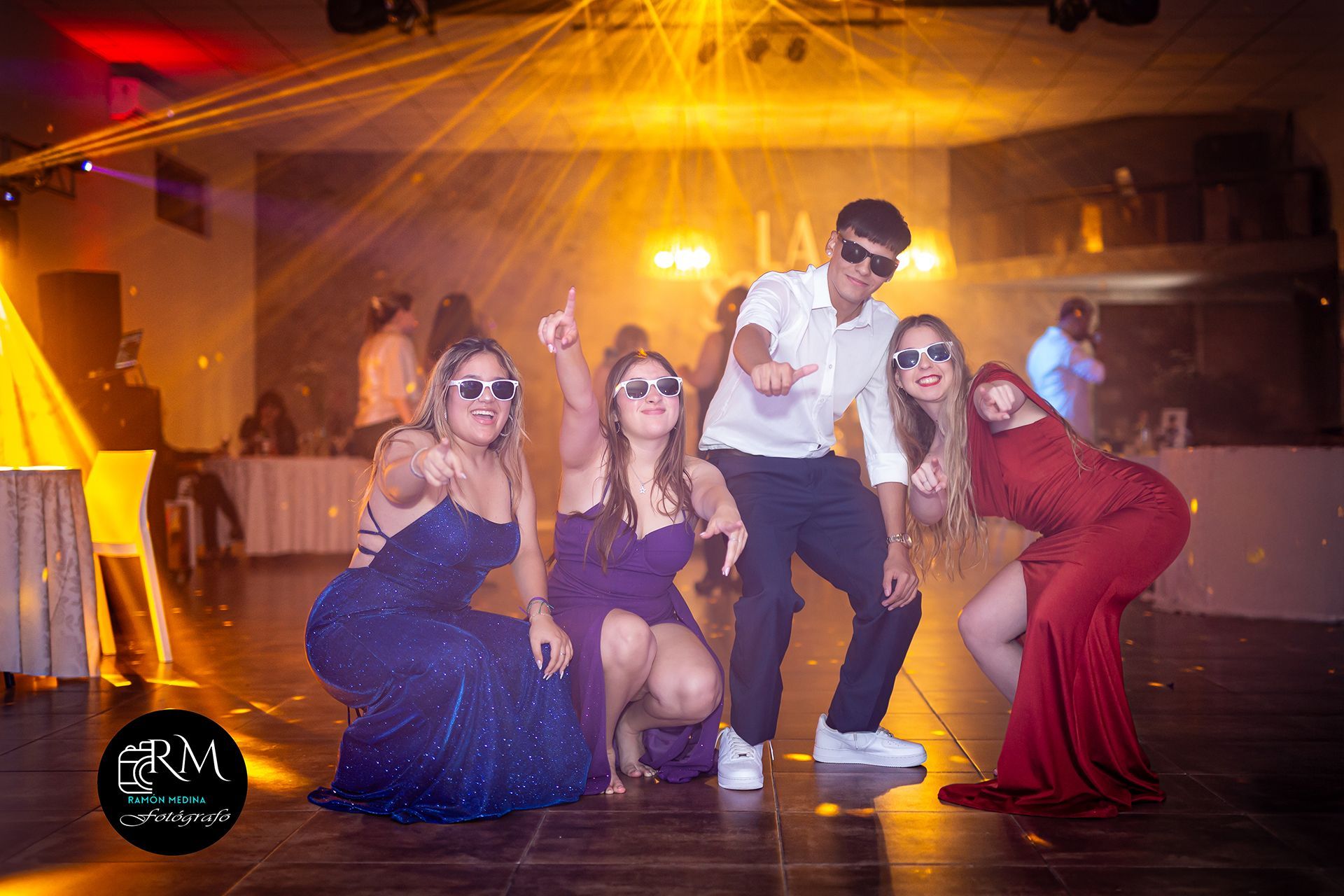 Cuatro personas posan dramáticamente en una pista de baile, iluminada por luces de escenario.