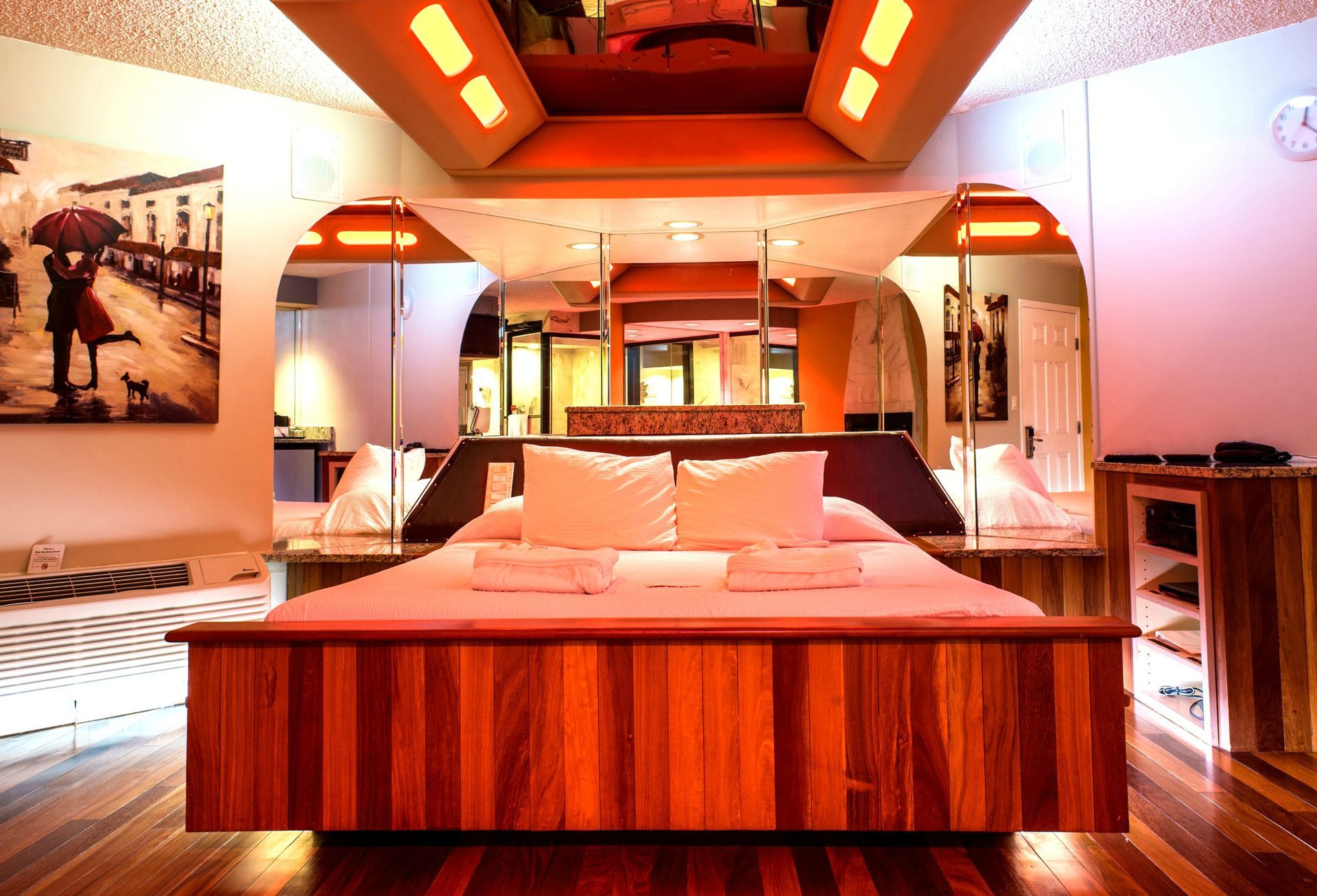 Hotel room with a bed, mirrors, and dim orange lighting.