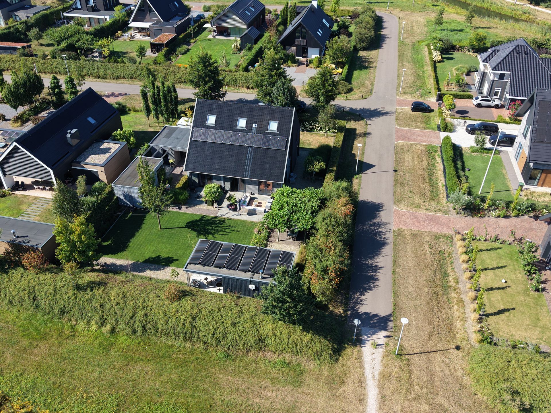Luchtfoto van huizen in een buitenwijk met tuinen langs een onverharde weg en grasvelden.