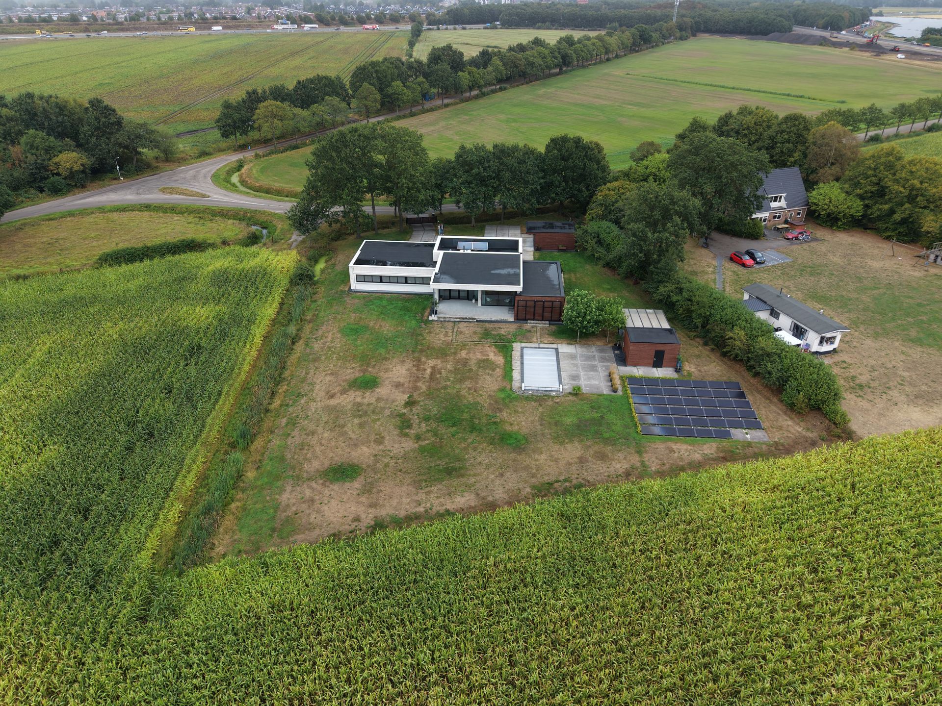 Luchtfoto van een boerderij met zonnepanelen, velden en een kronkelende landweg.