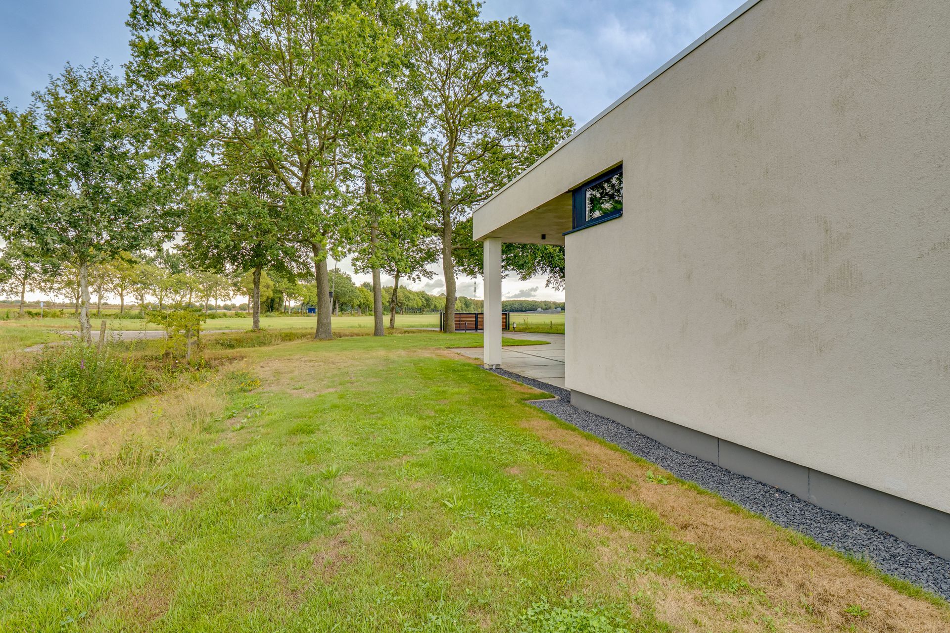 Grasveld naast een wit gebouw met bomen en een meer op de achtergrond.